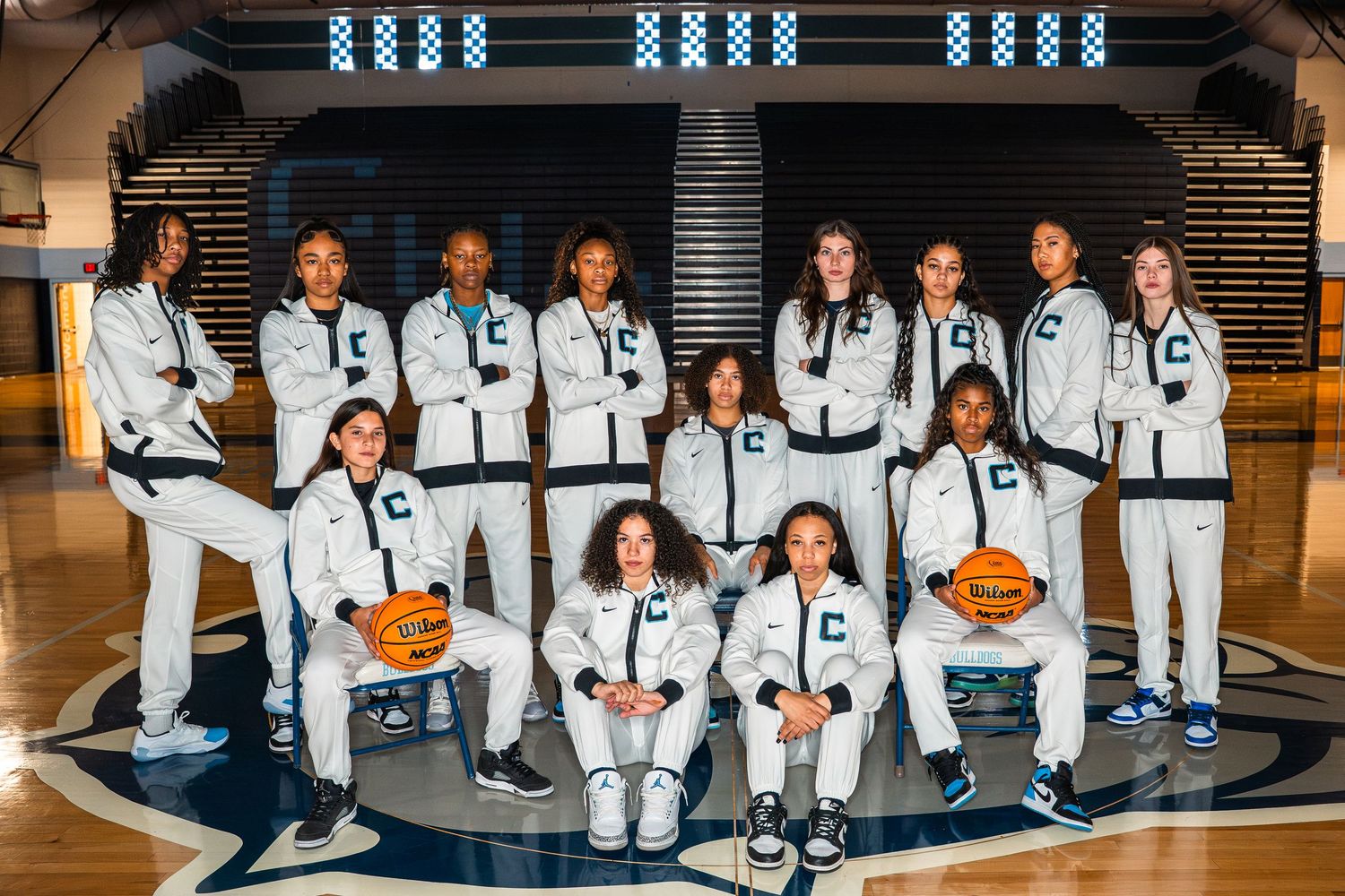 Basketball team members pose together in white uniforms on gym floor with orange ball.