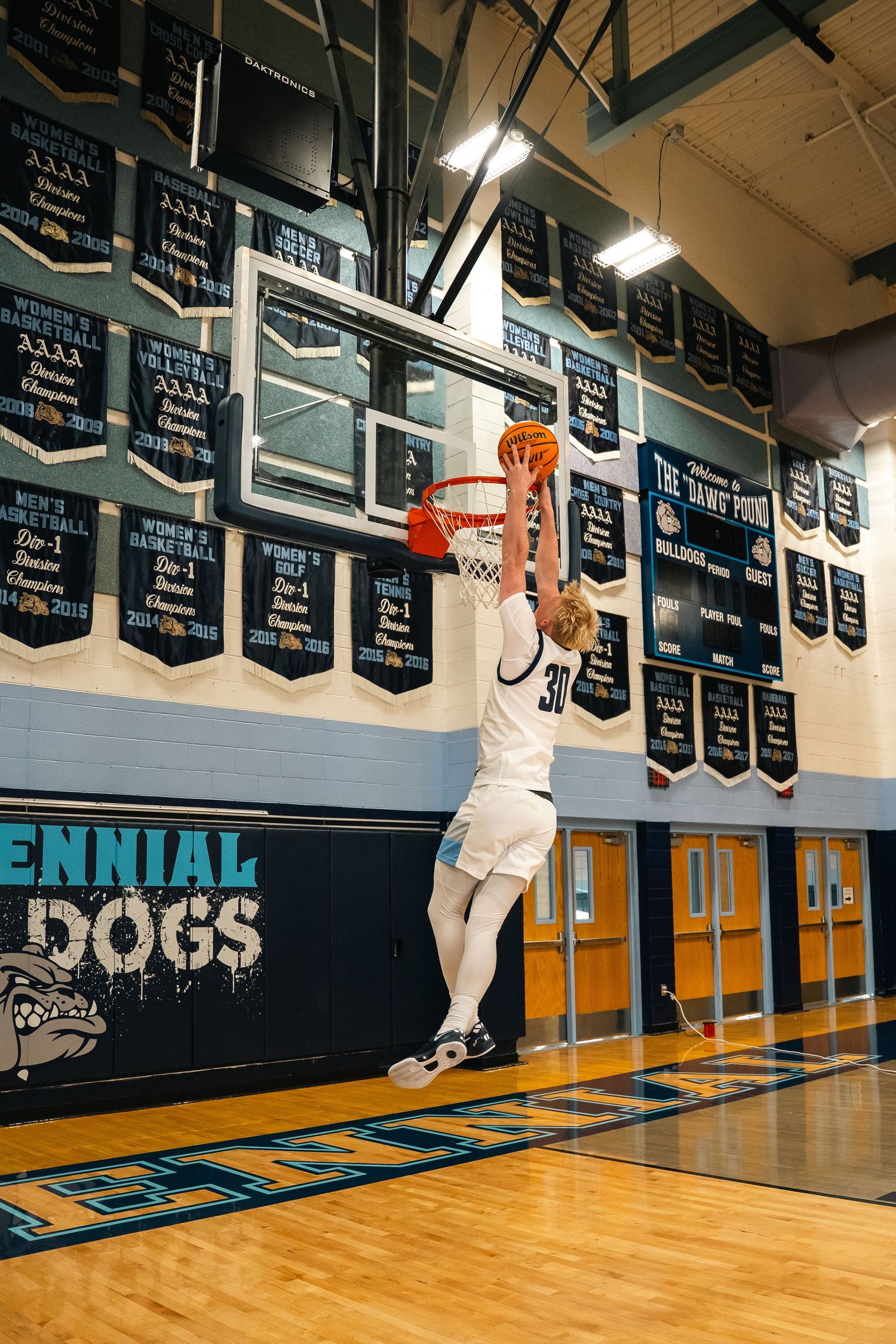 Basketball player in white uniform going for layup under championship banners.