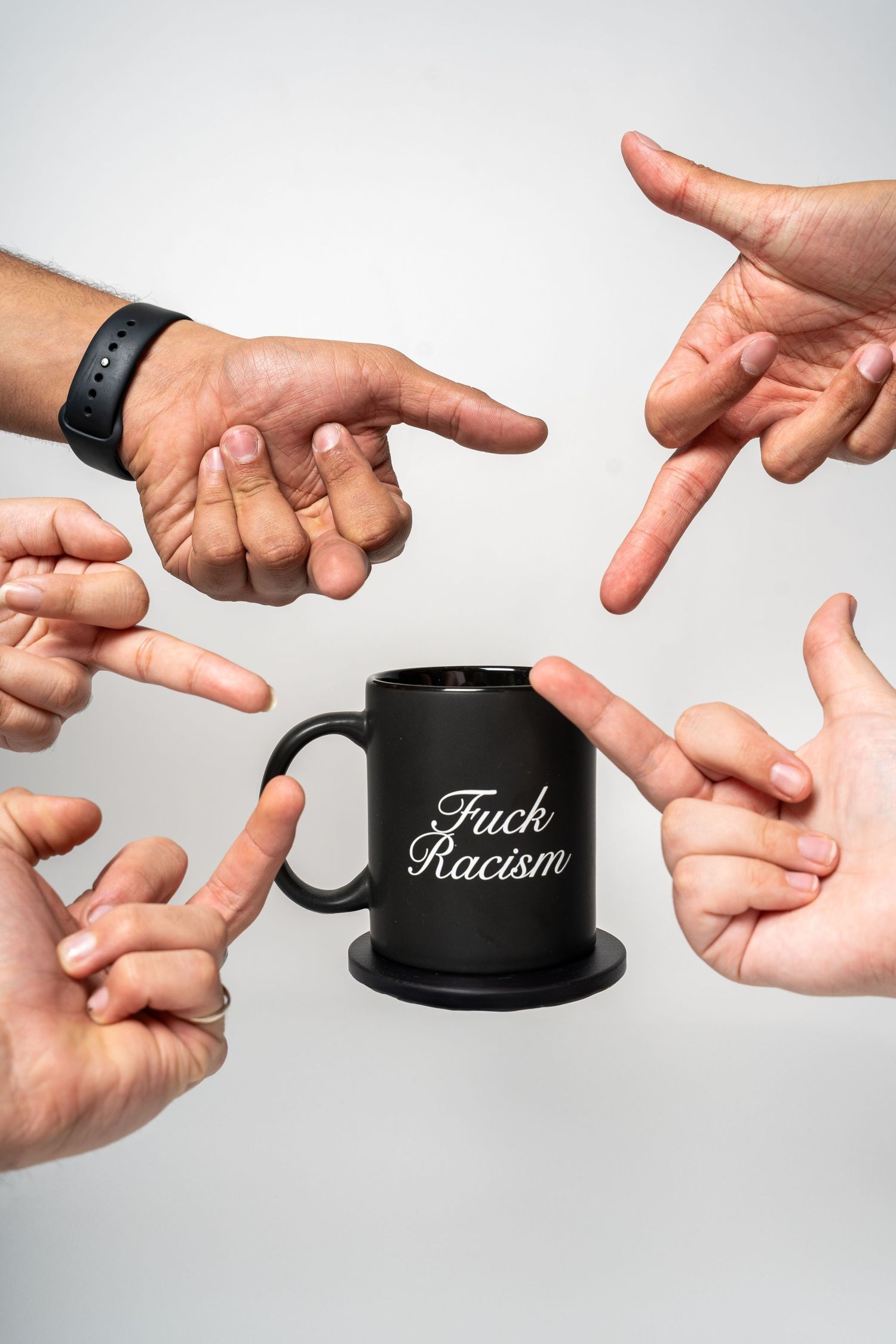 Multiple hands pointing at black coffee mug with social justice message against white background.