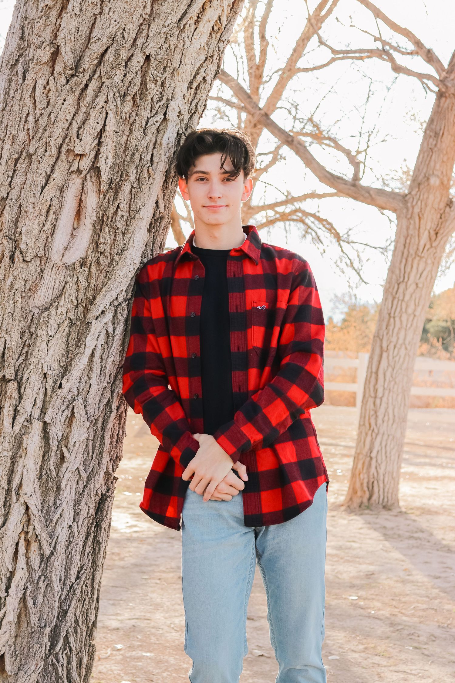 Portrait against tree trunk wearing red buffalo check flannel shirt.