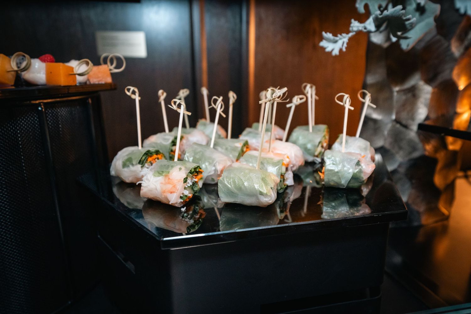 Elegant appetizers arranged on black display stands with decorative toothpicks at an upscale event.