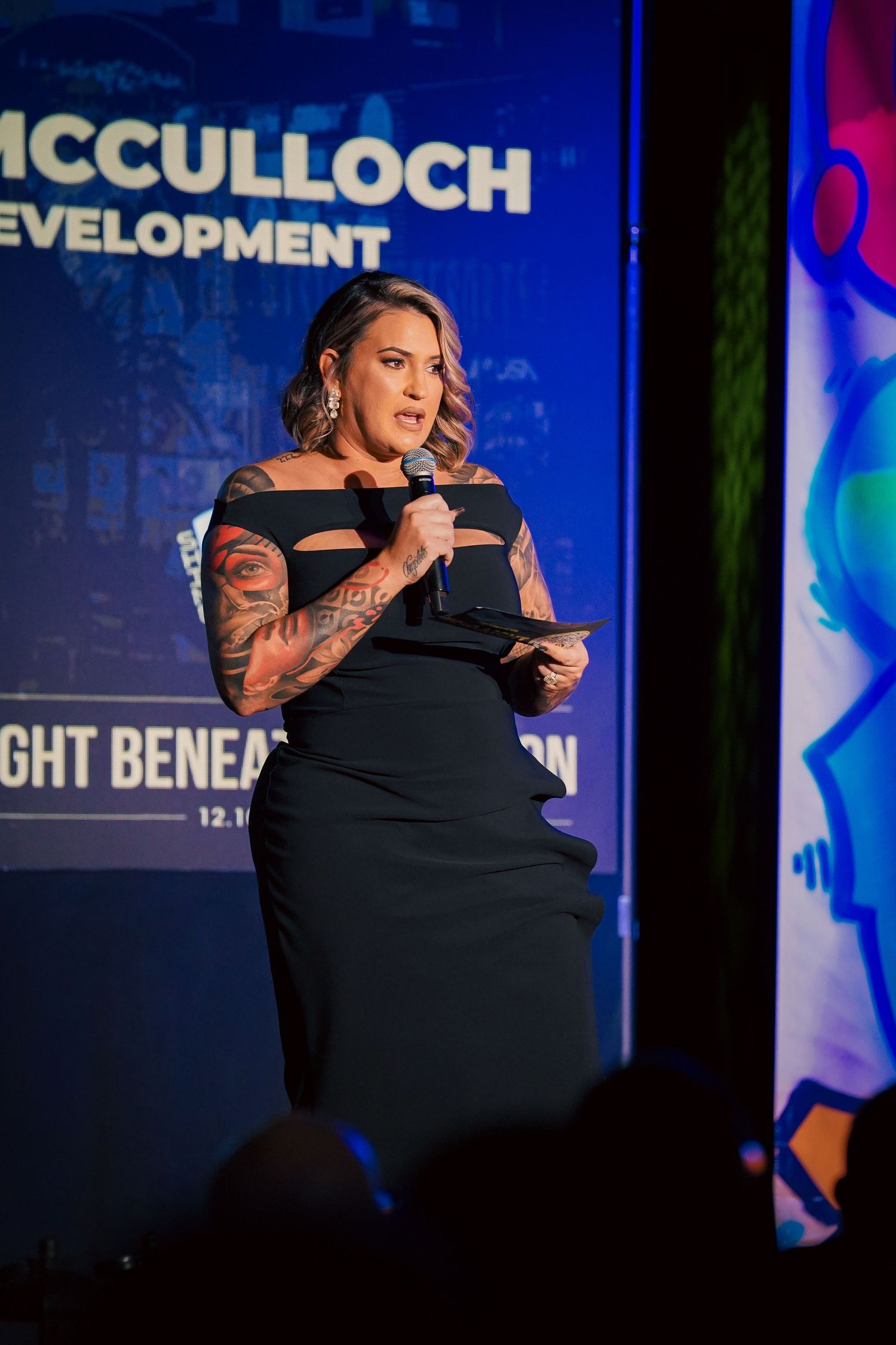 Speaker in black dress presenting on stage at a McCulloch Development benefit event.