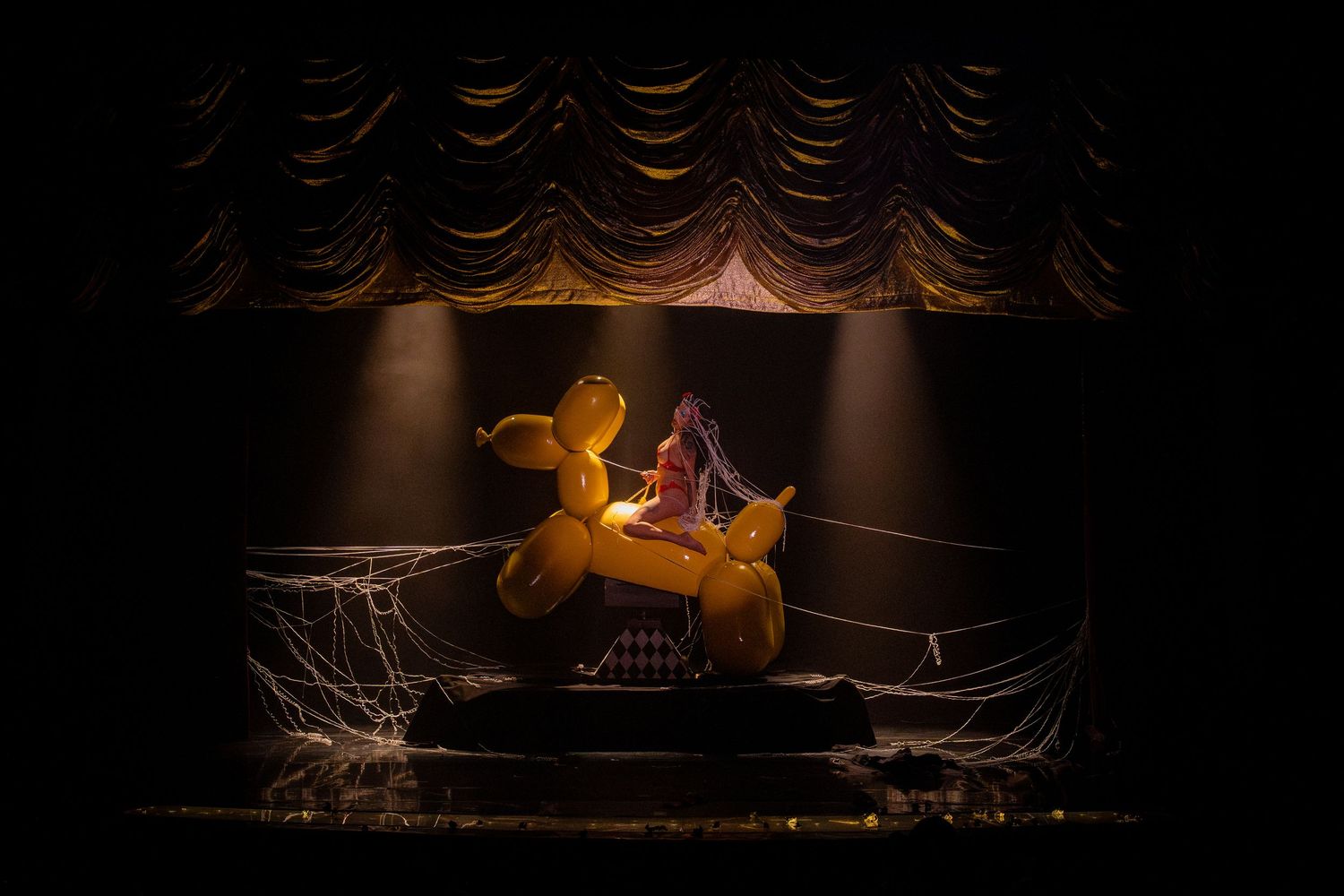 Whimsical stage performance featuring yellow prop motorcycle under dramatic spotlight.