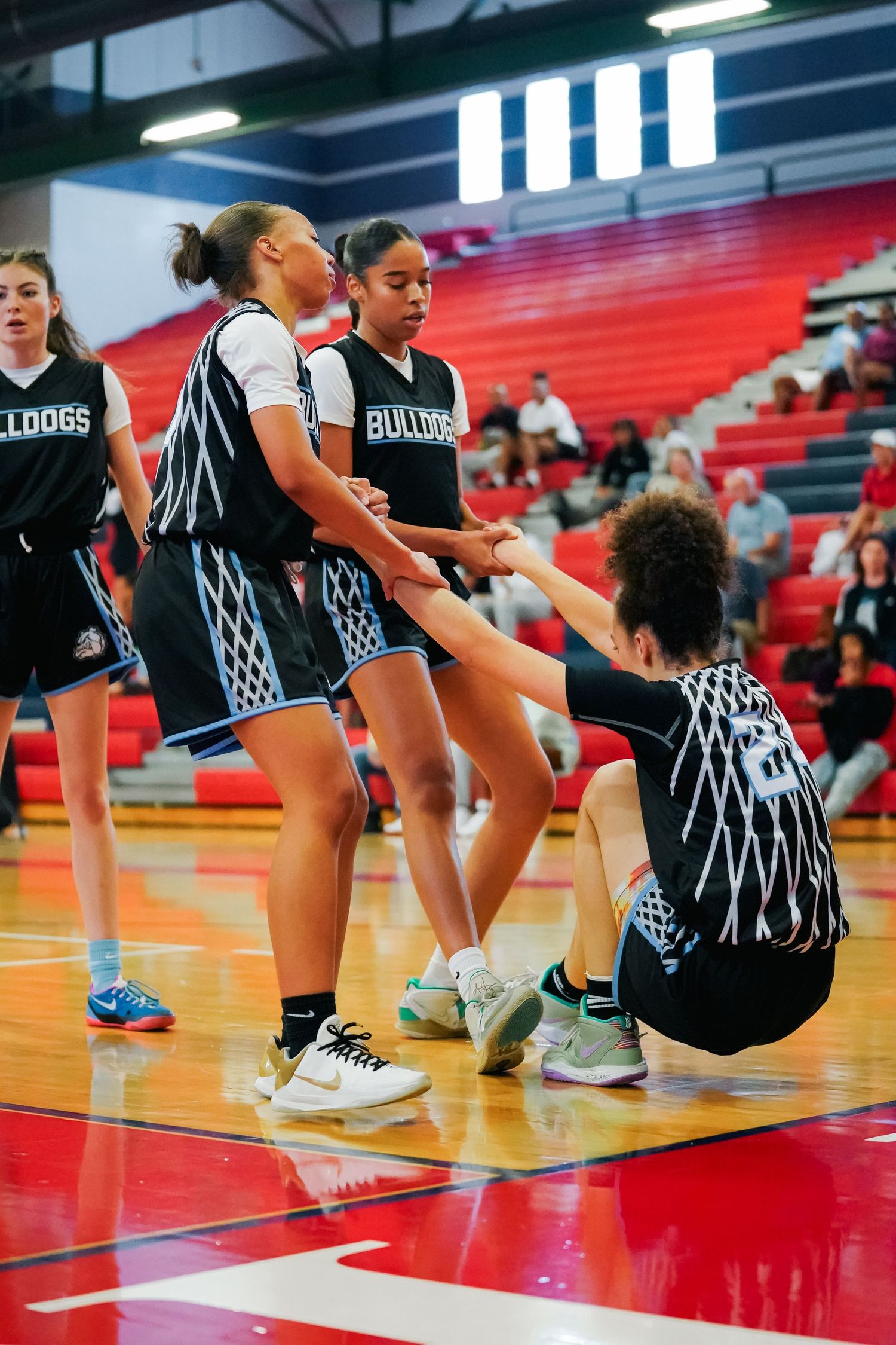 Basketball team in matching black uniforms stretches together on red gymnasium floor.
