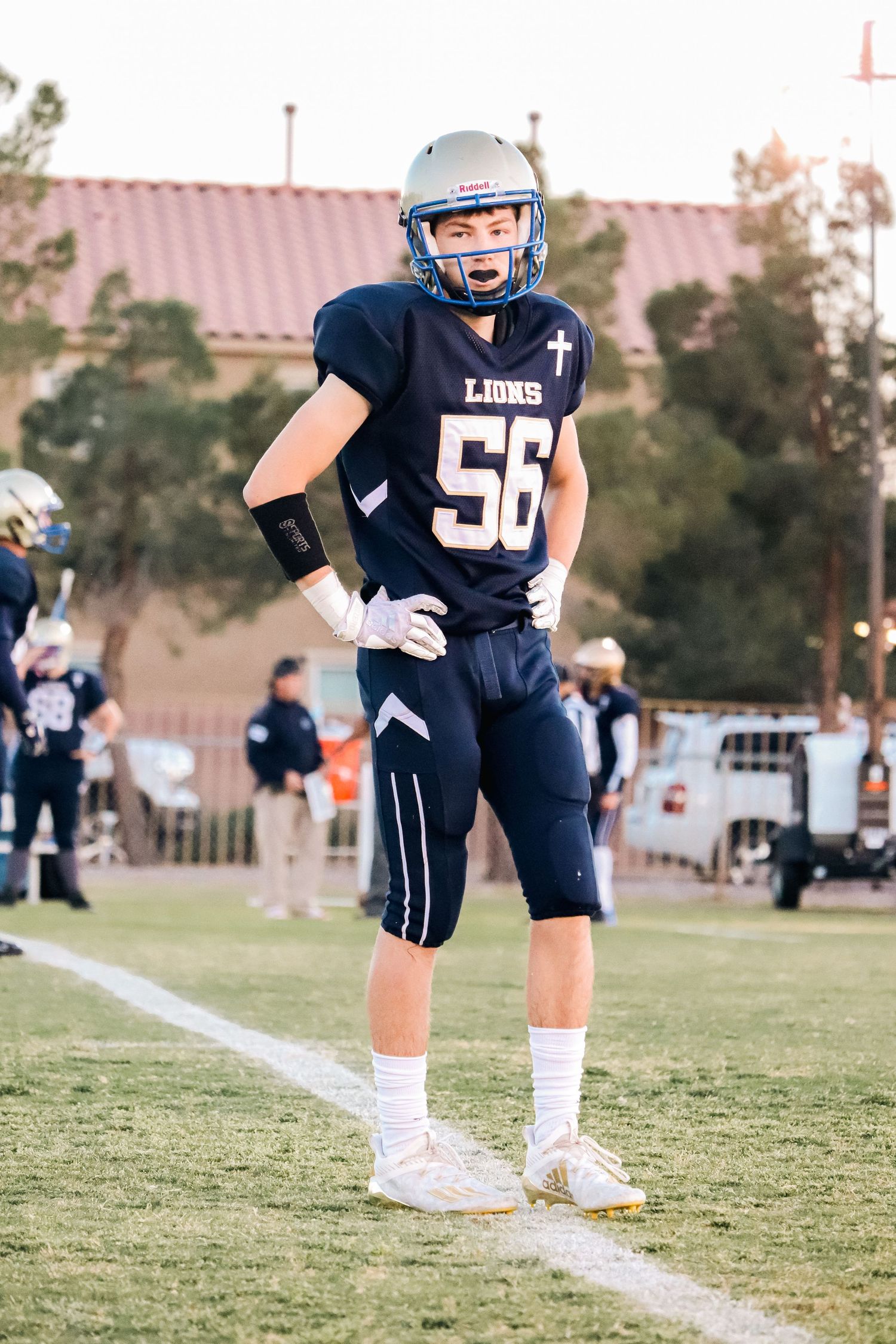 Football player in navy uniform with number 56 stands on sideline during game.