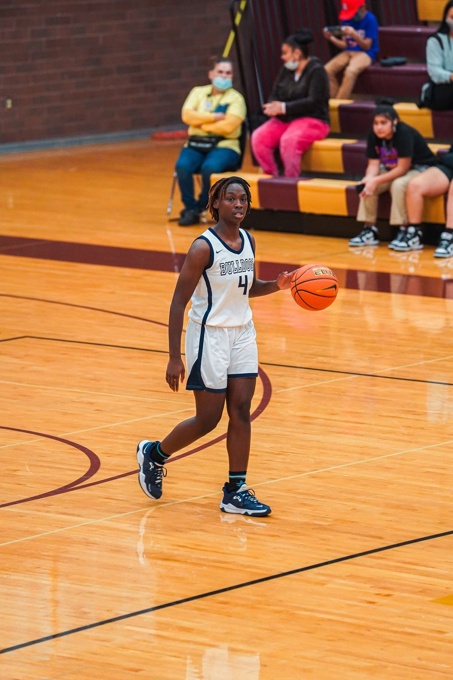 Basketball player in white uniform dribbles the ball on wooden court during game.