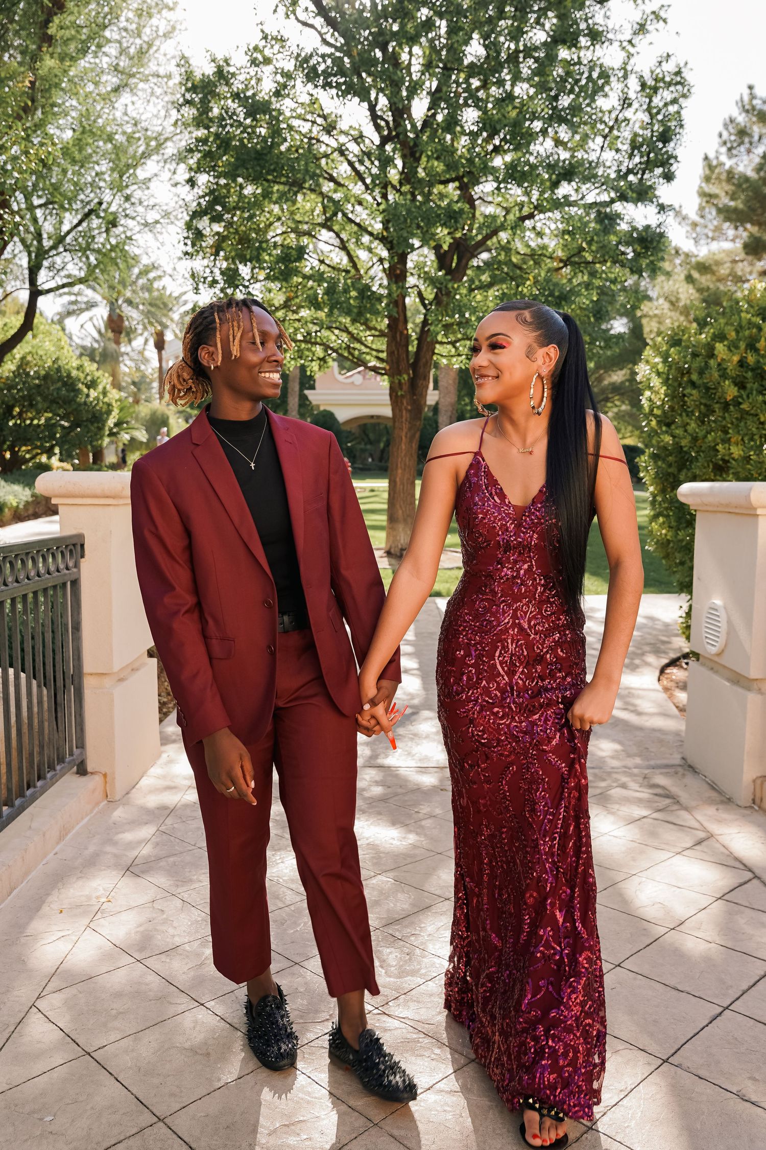 Couple in matching burgundy attire holding hands on elegant stone patio.