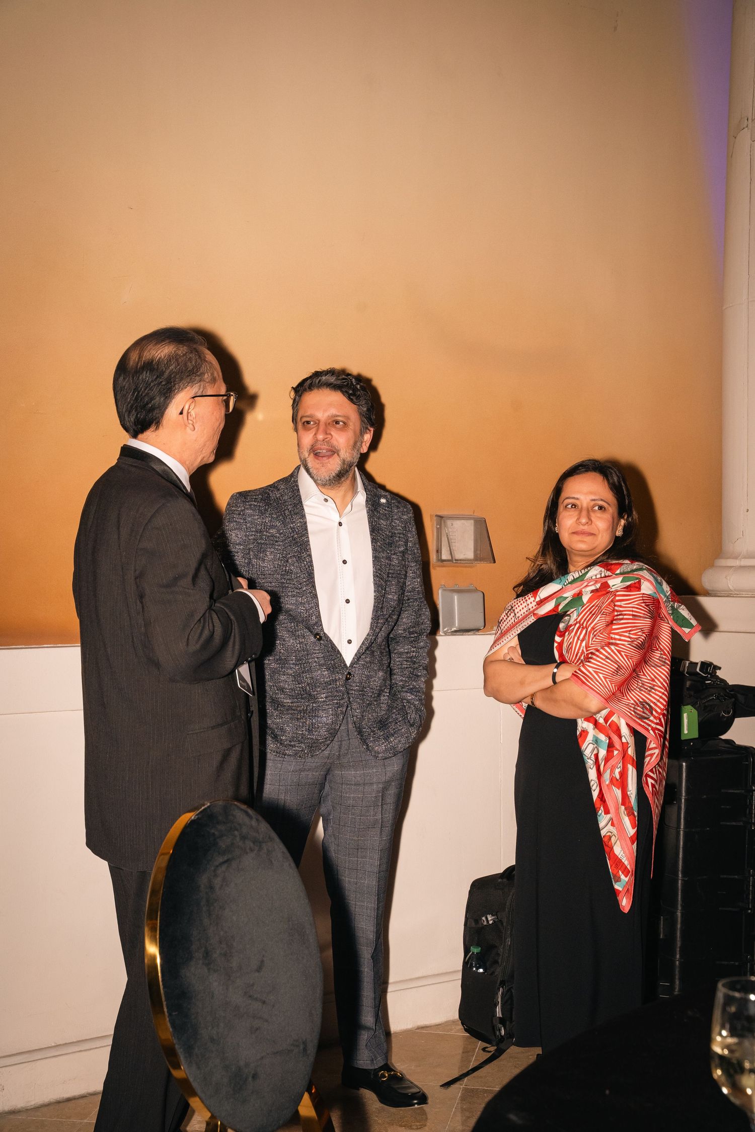 Three attendees engage in conversation during an evening business networking event.
