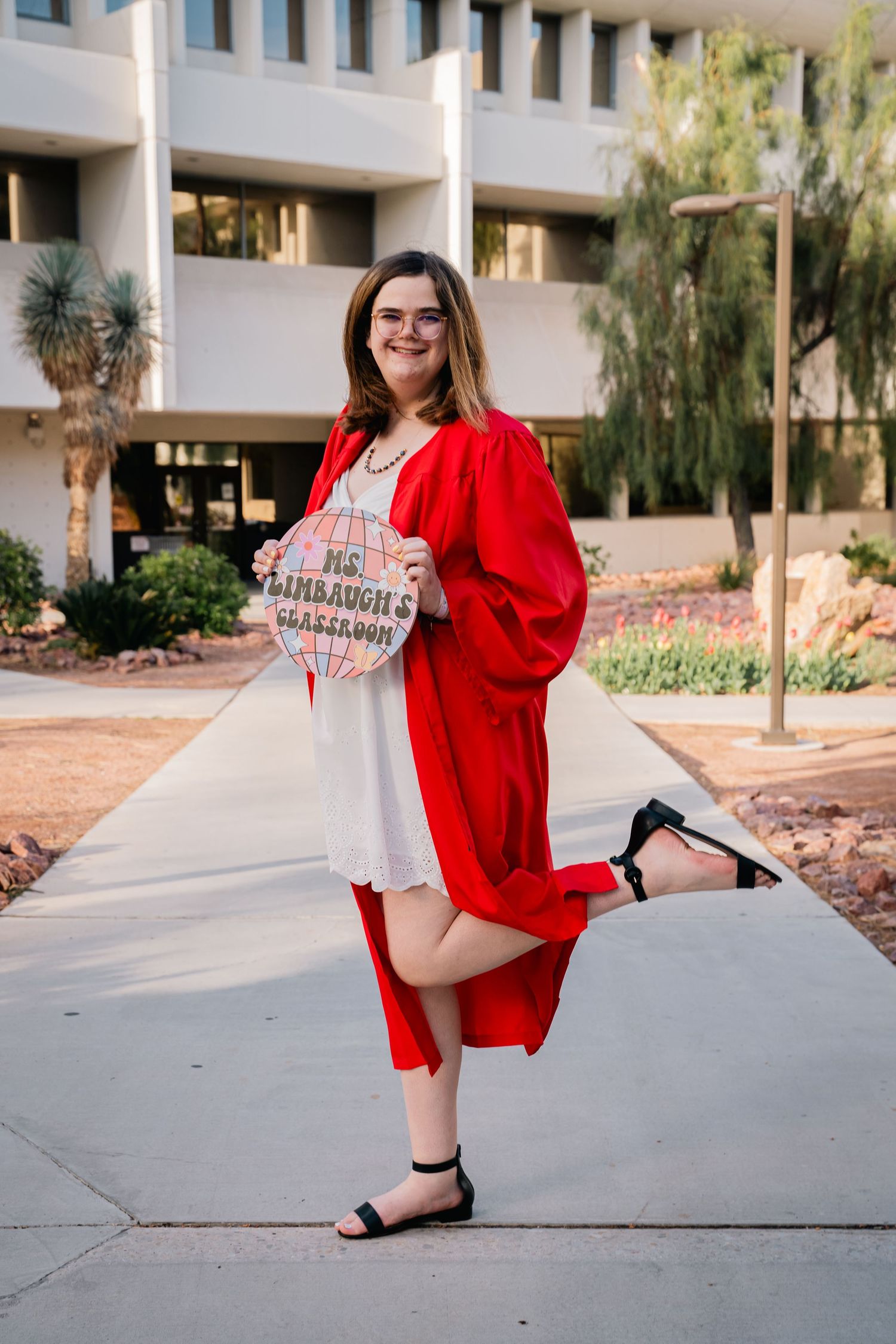 Graduate in bright red regalia poses with decorated cap outside academic building.