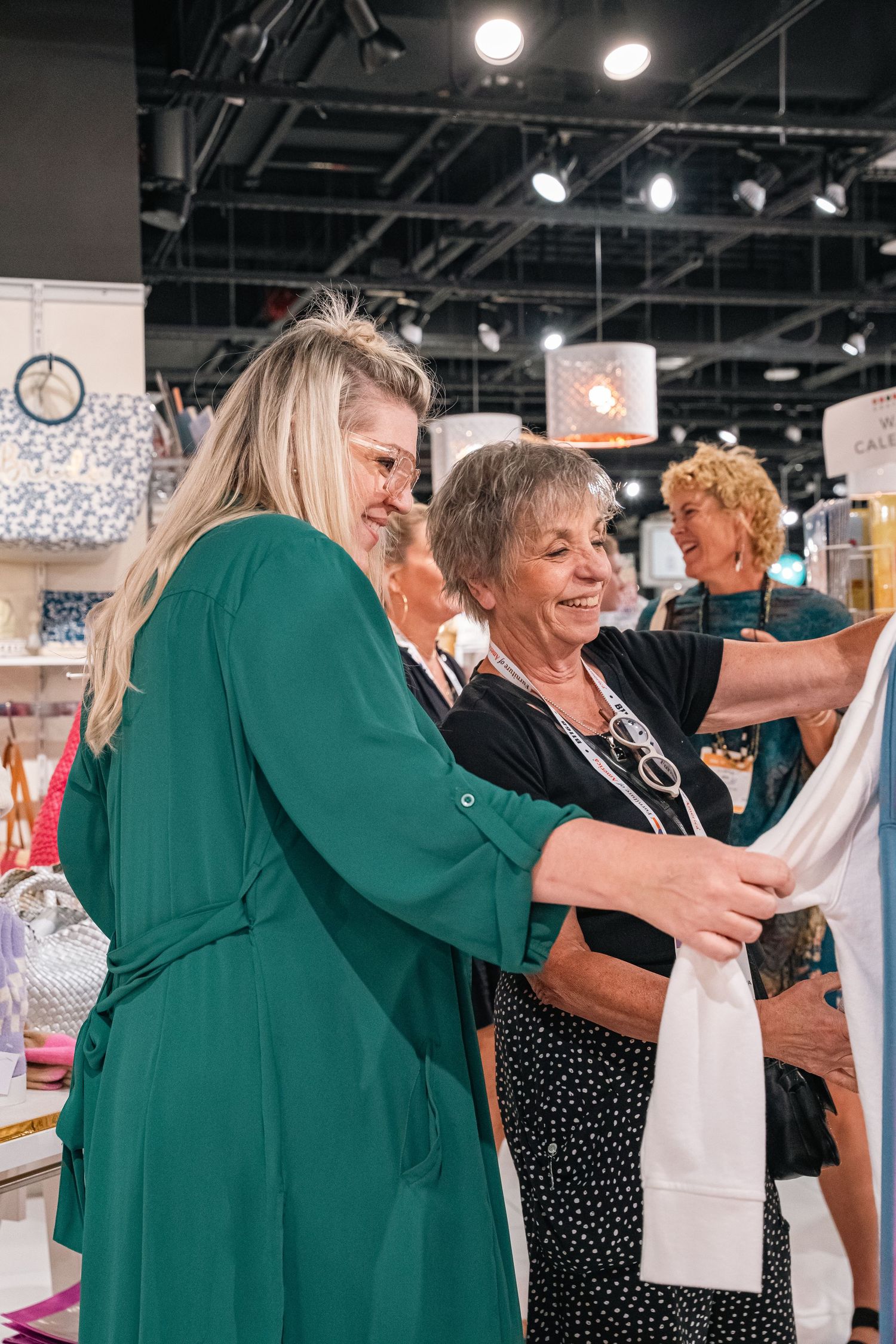 Customers examine clothing items together in a well-lit retail store with hanging lights and merchandise displays.