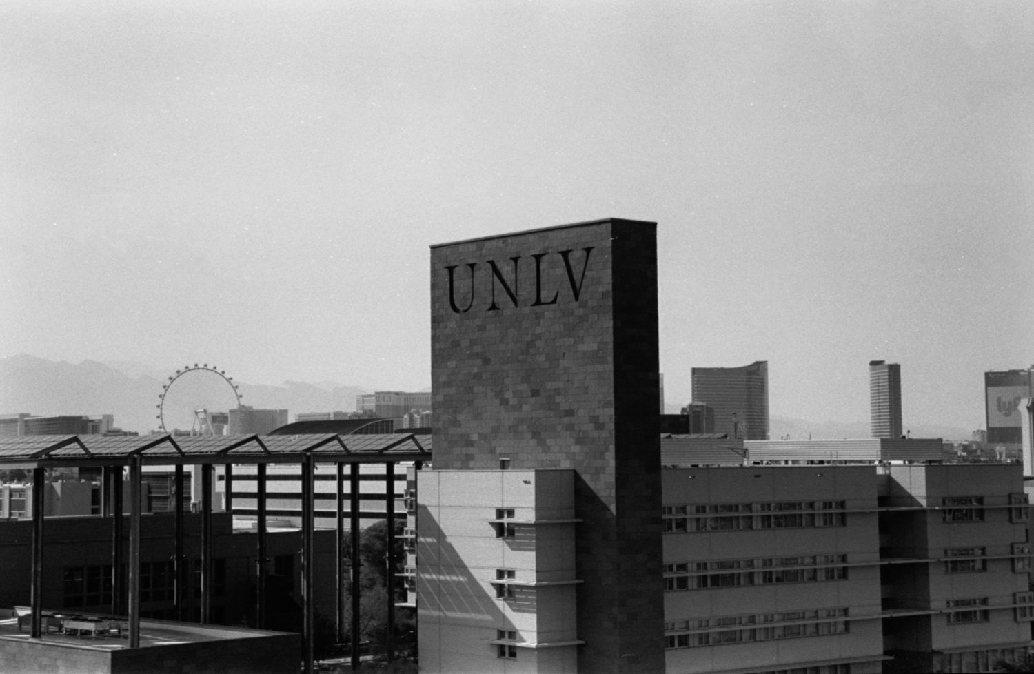 UNLV campus buildings with ferris wheel visible in background against black and white cityscape.