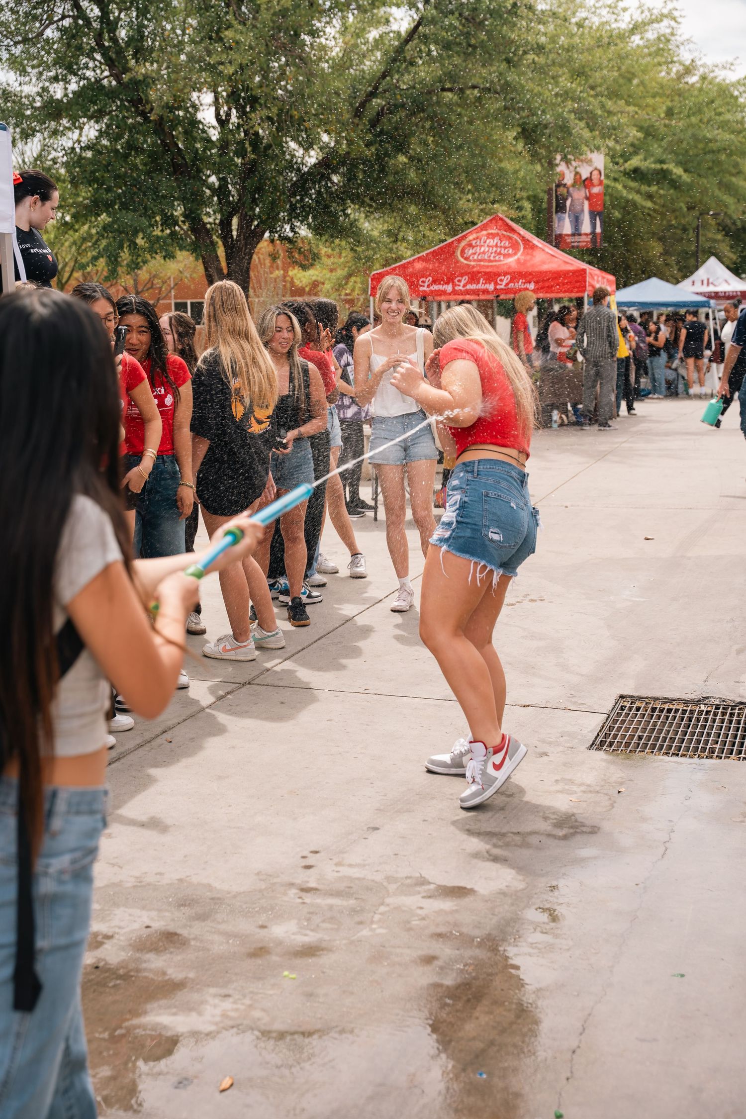 Student doing limbo under blue pole at outdoor campus festival.