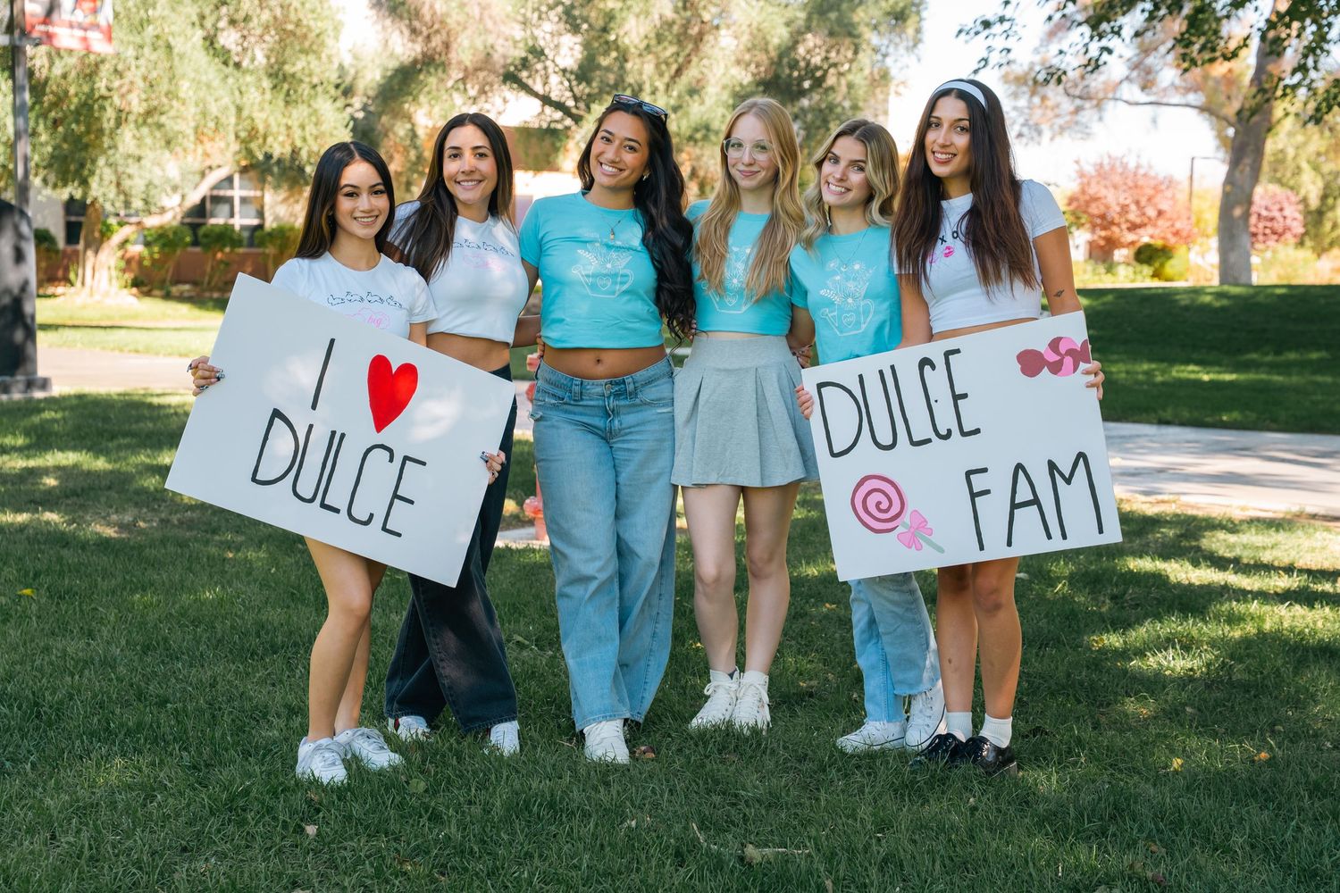 Group of sorority sisters in light blue outfits hold Dulce themed signs while posing outdoors.