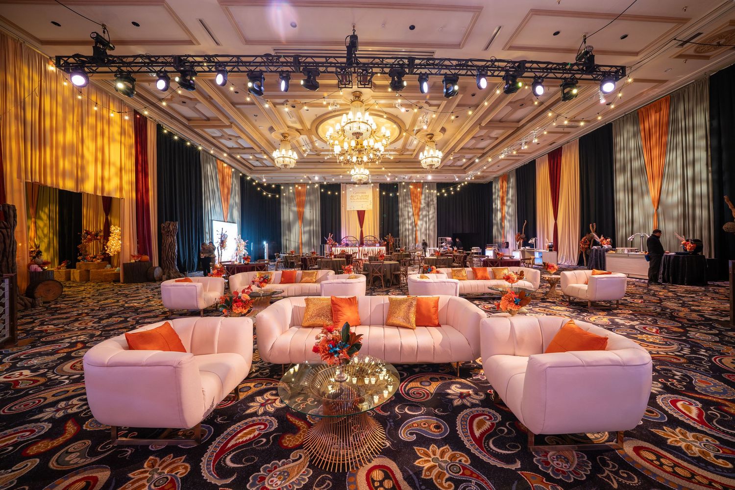 Modern lounge area with white circular seating and ornate chandelier in casino ballroom.
