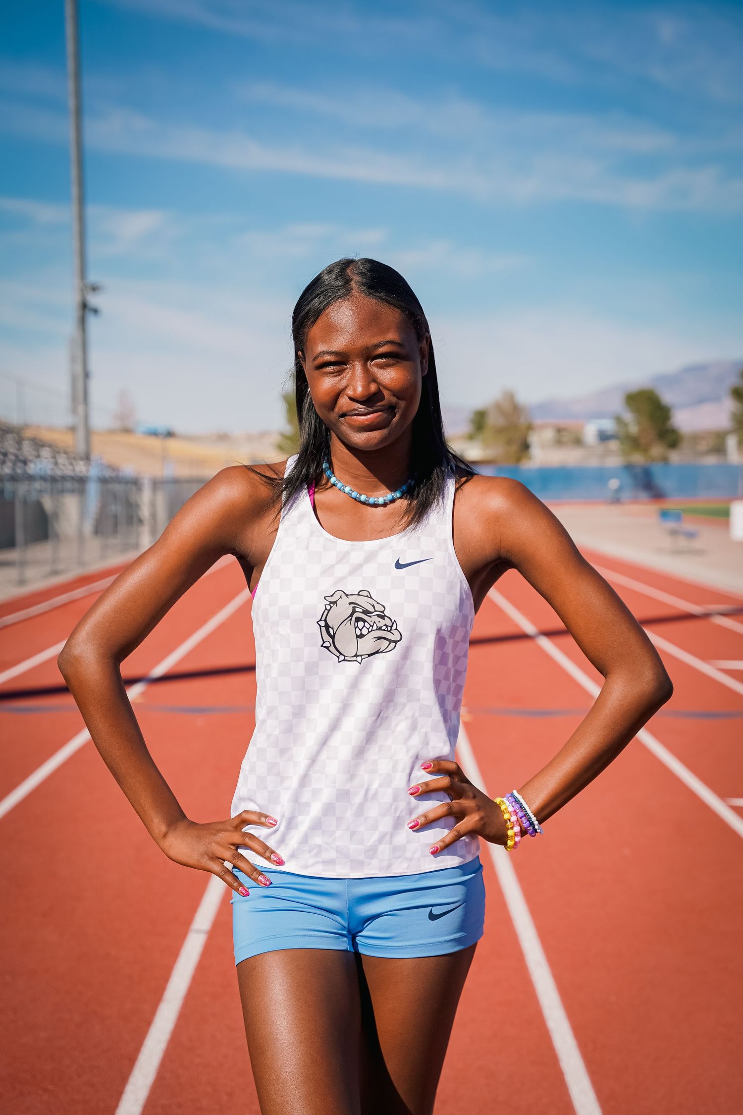 Athlete in white tank top poses on red running track.