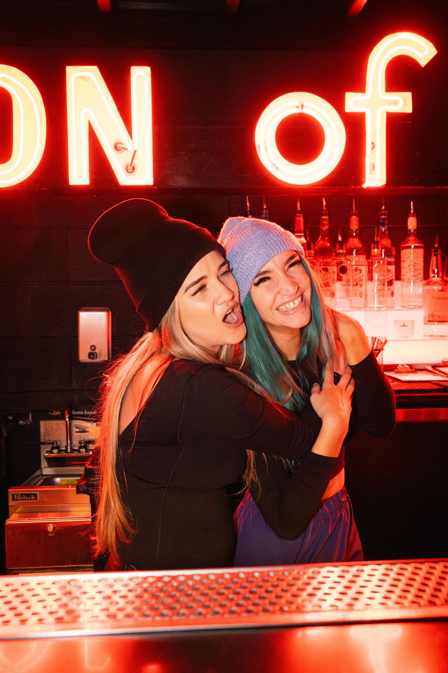 Friends having fun at bar counter with neon 'ON OF' sign glowing in background.