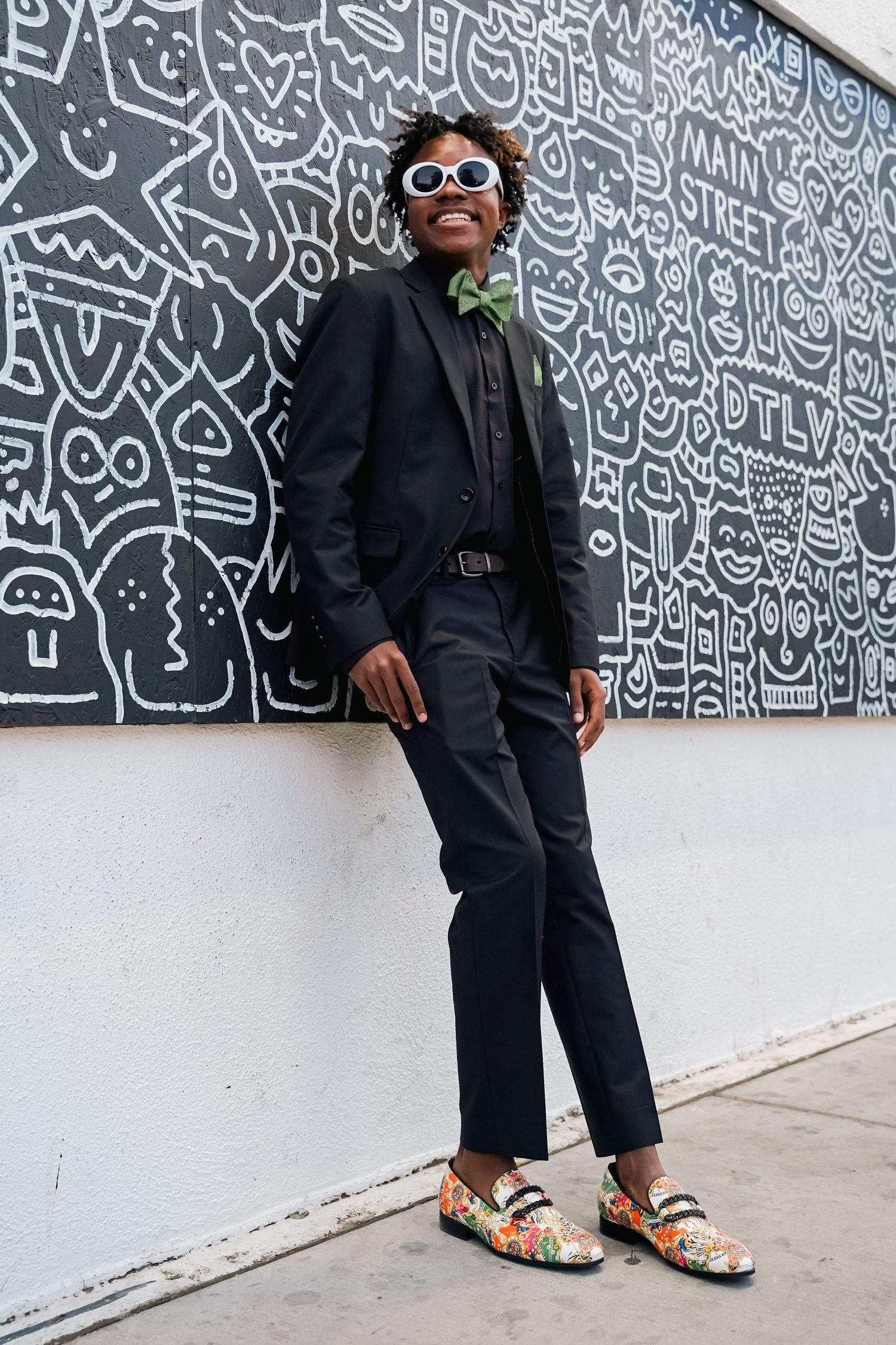 Men in dark suits and white sunglasses posing by a wall with graphic art patterns.