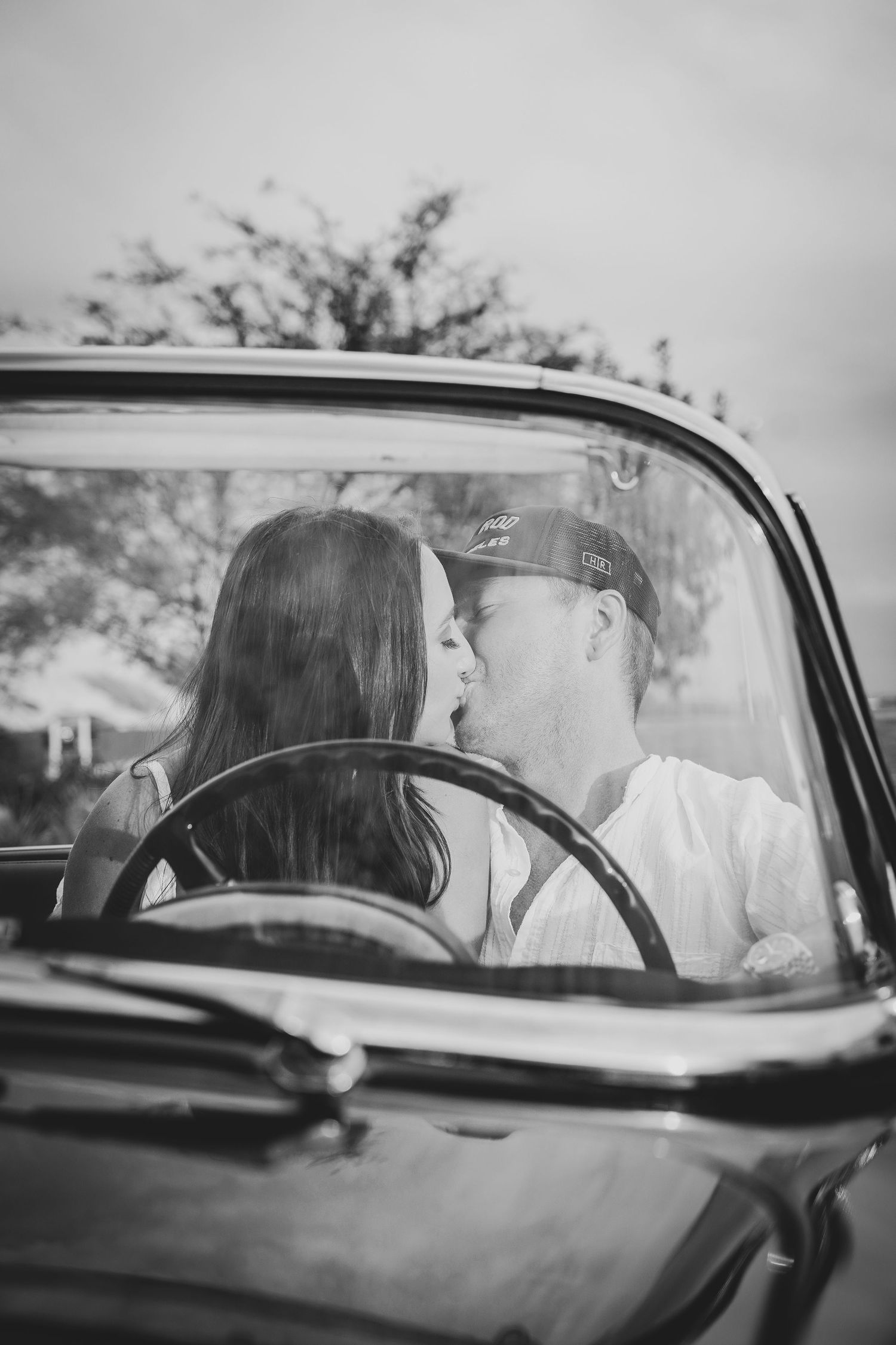 Black and white photo of a couple sharing a romantic moment in a vintage car.