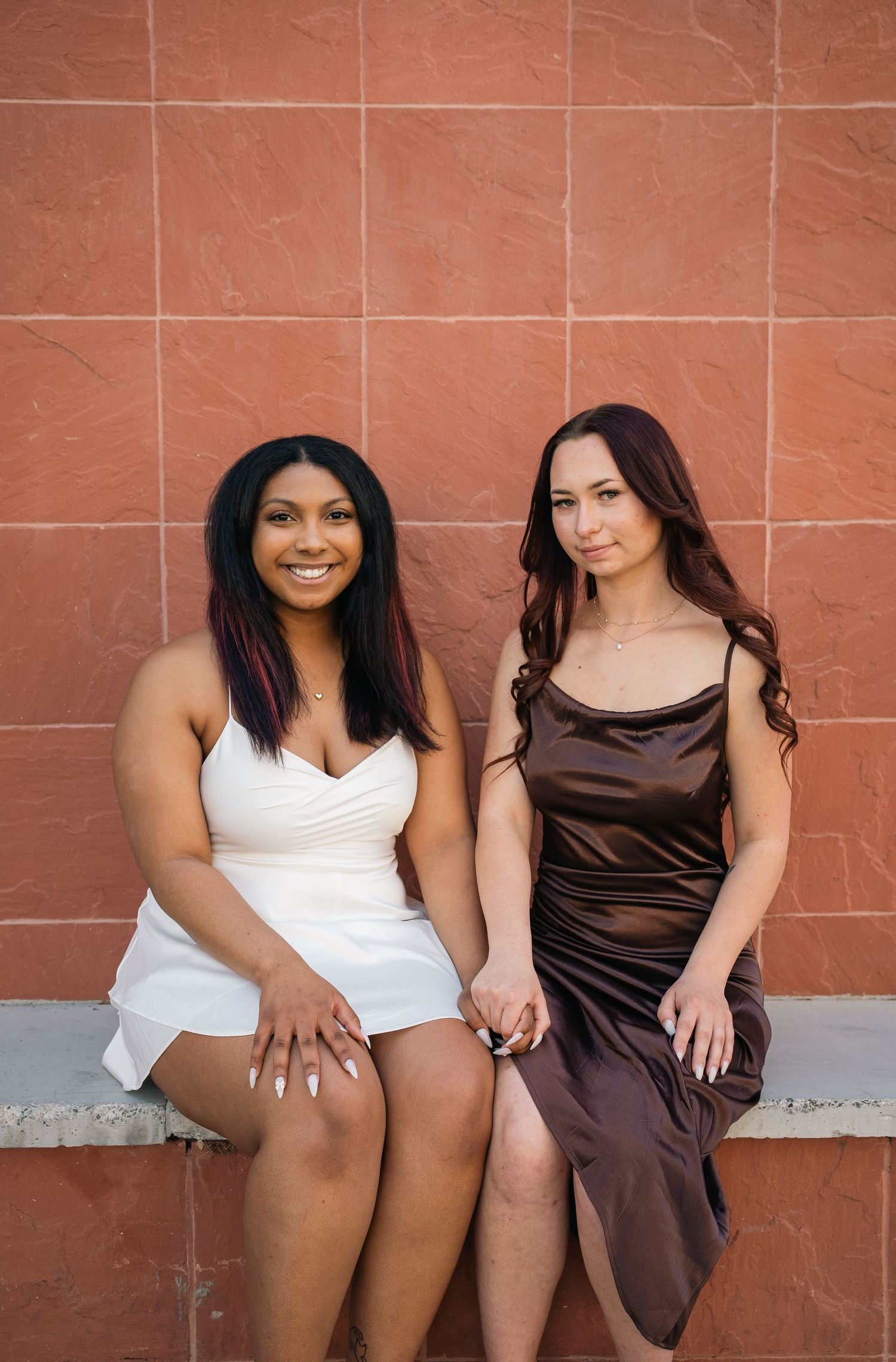 Two friends sitting together wearing contrasting white and brown formal dresses.