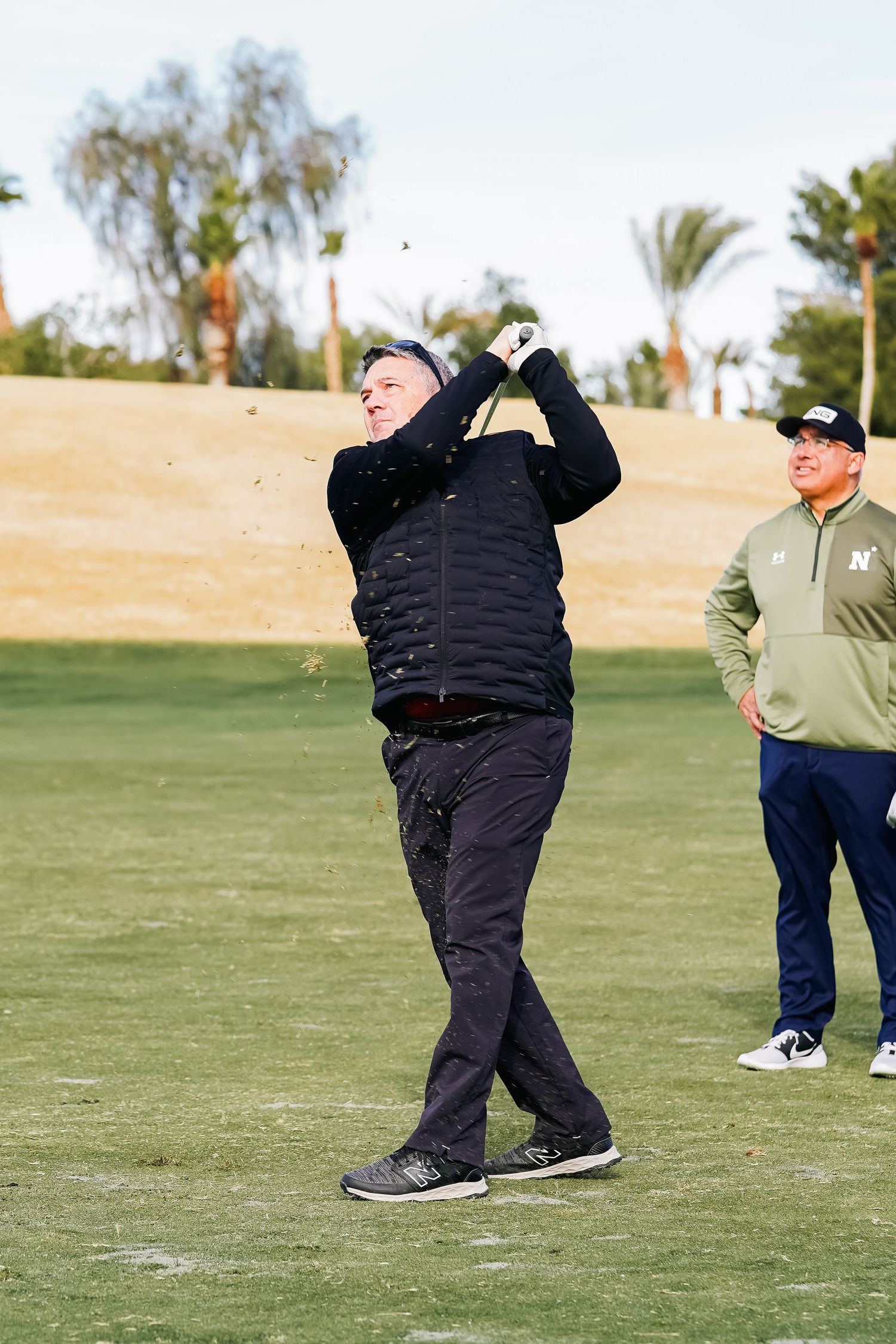 Golfers practicing their swings on a sunny golf course with palm trees.