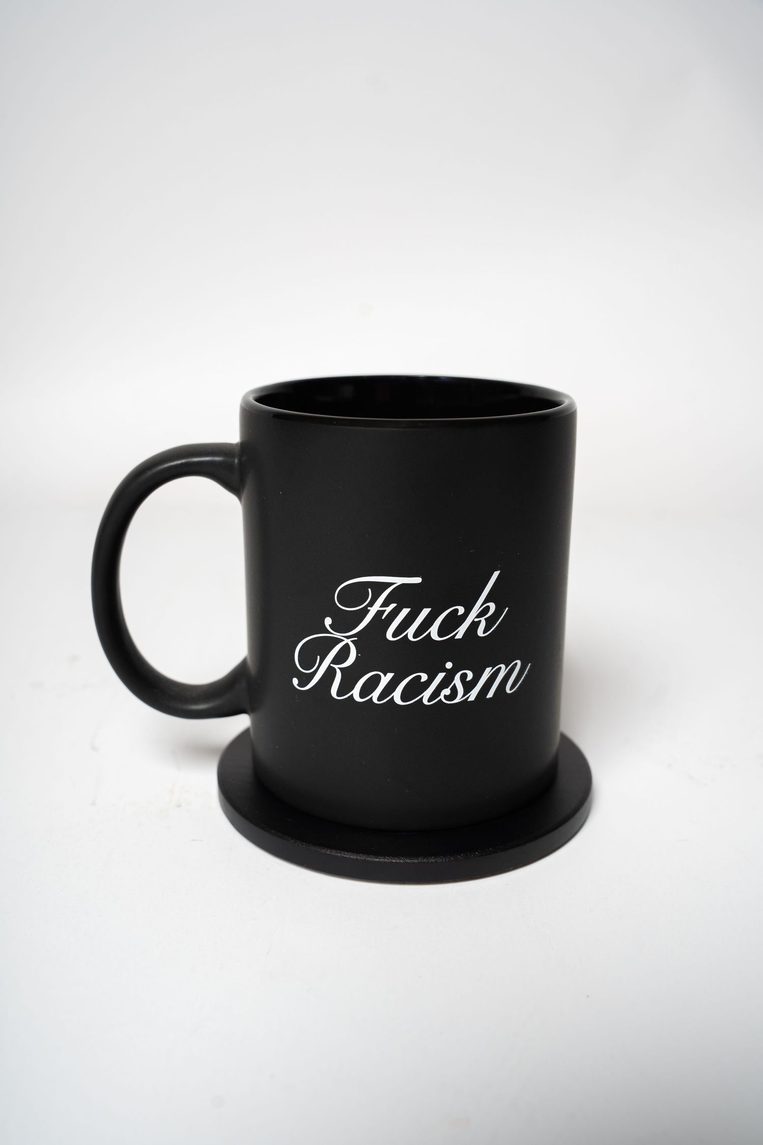 Black coffee mug with anti-racism message on black coaster against white background.