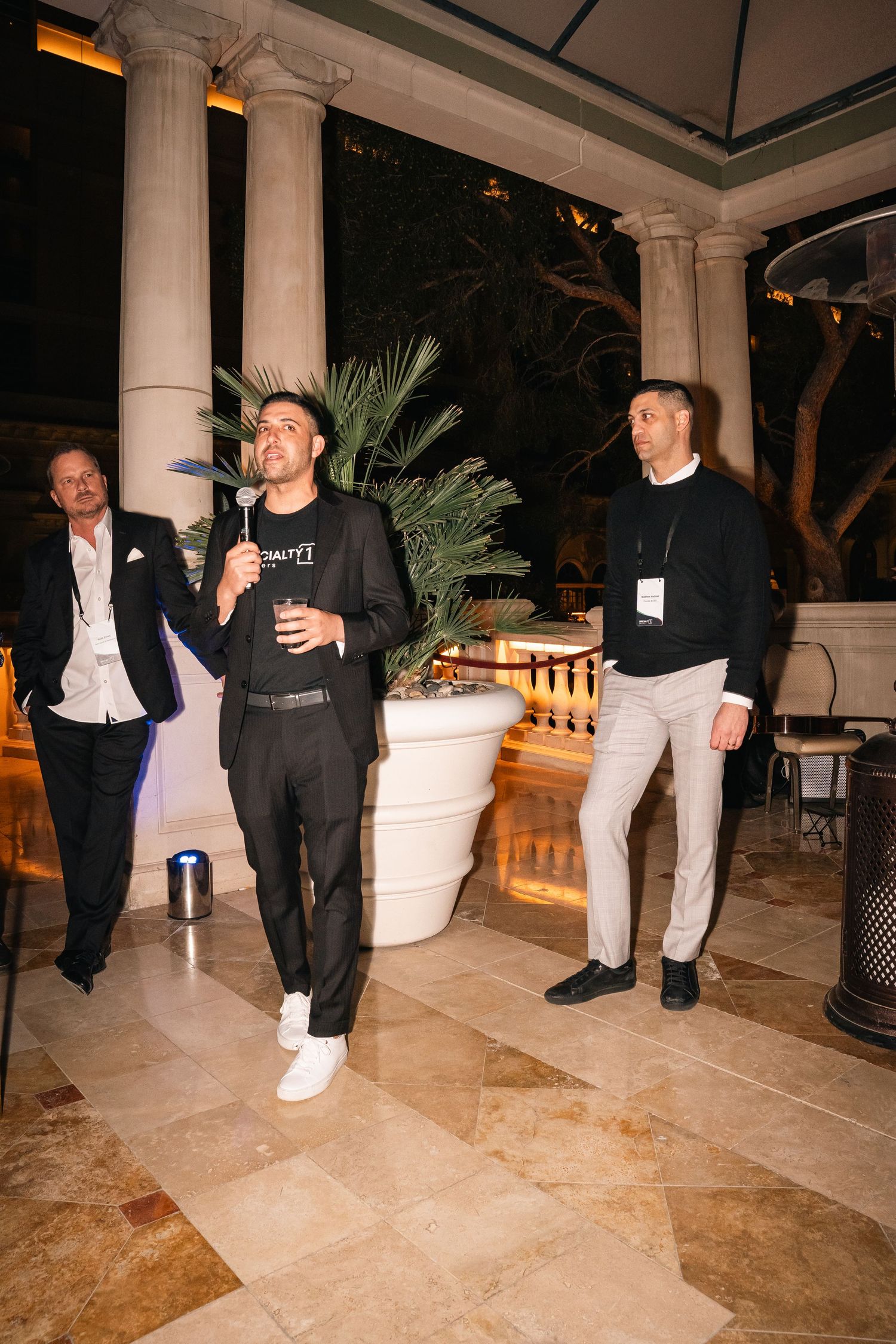 Guests socializing at an elegant venue with white columns and palm plants during evening event.