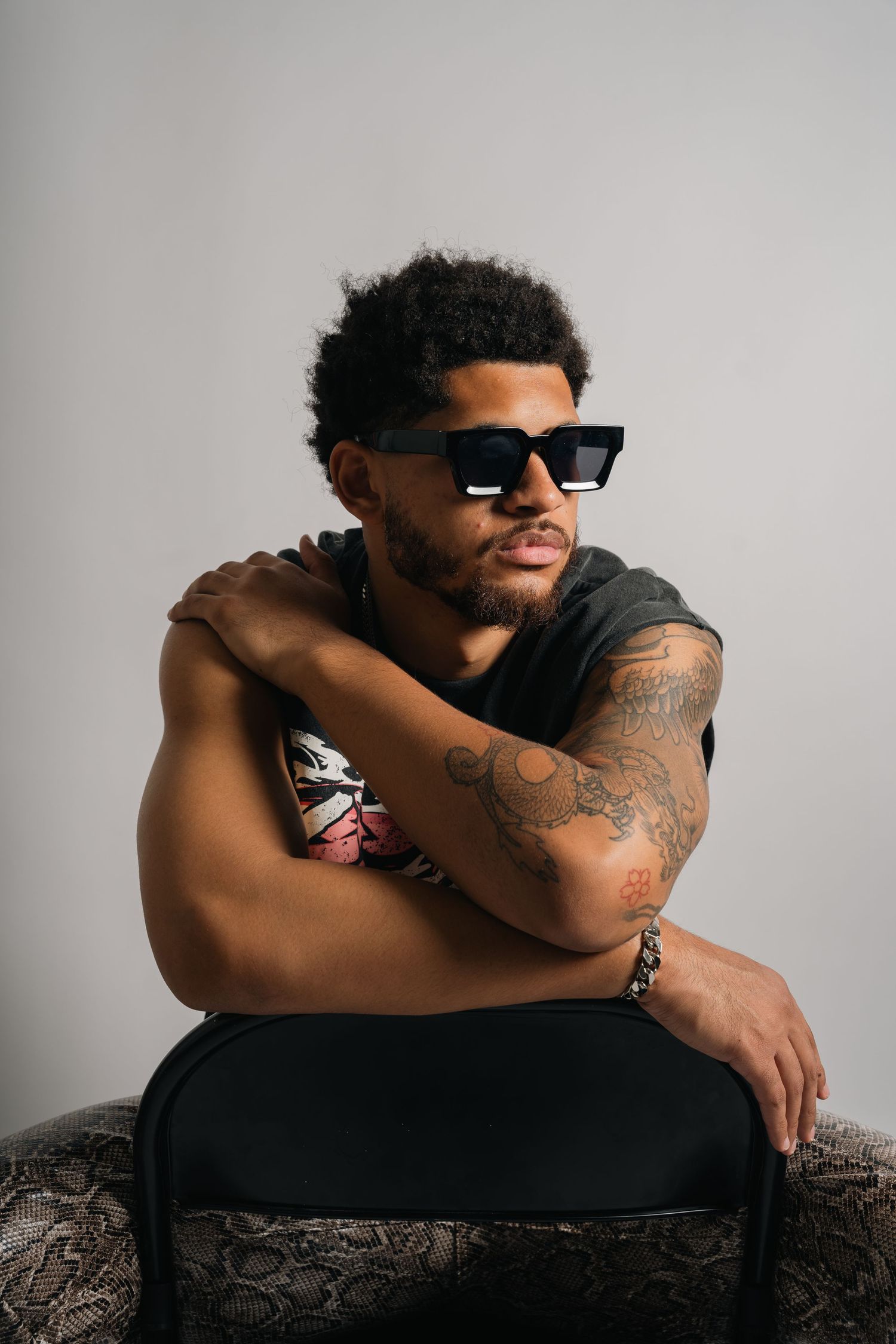 Artistic studio portrait of model in sunglasses posing on chair with crossed arms.