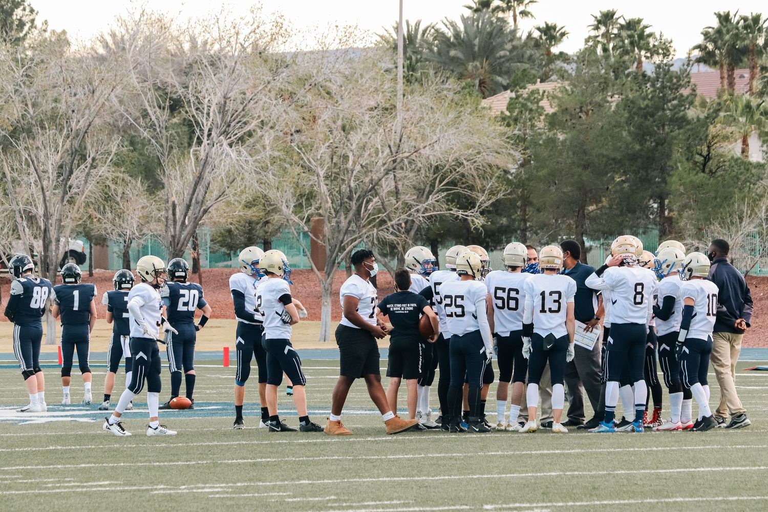 Football team gathers in huddle formation on sports field during practice.