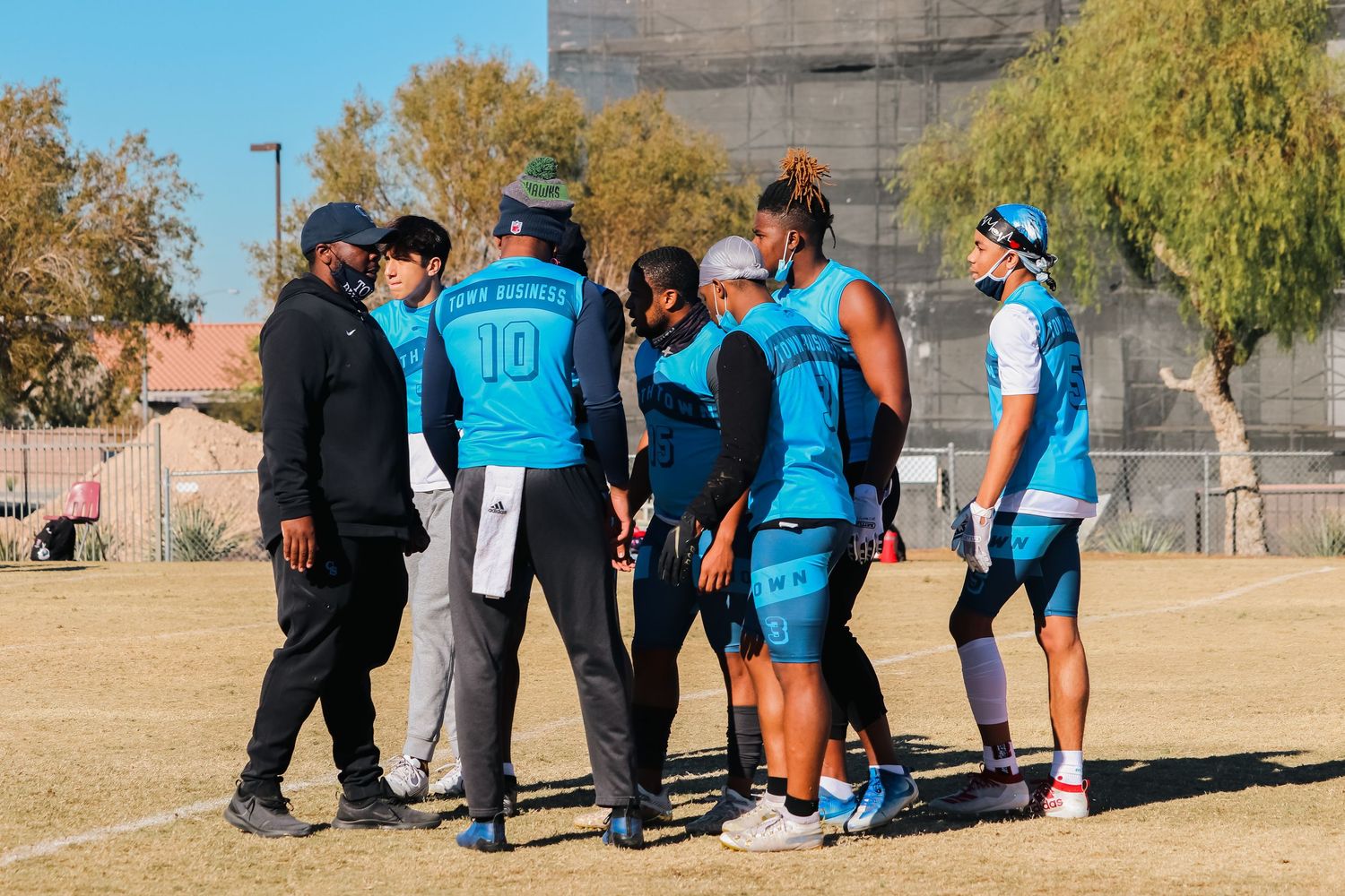 Team members in turquoise jerseys gathering on field during sports practice session.