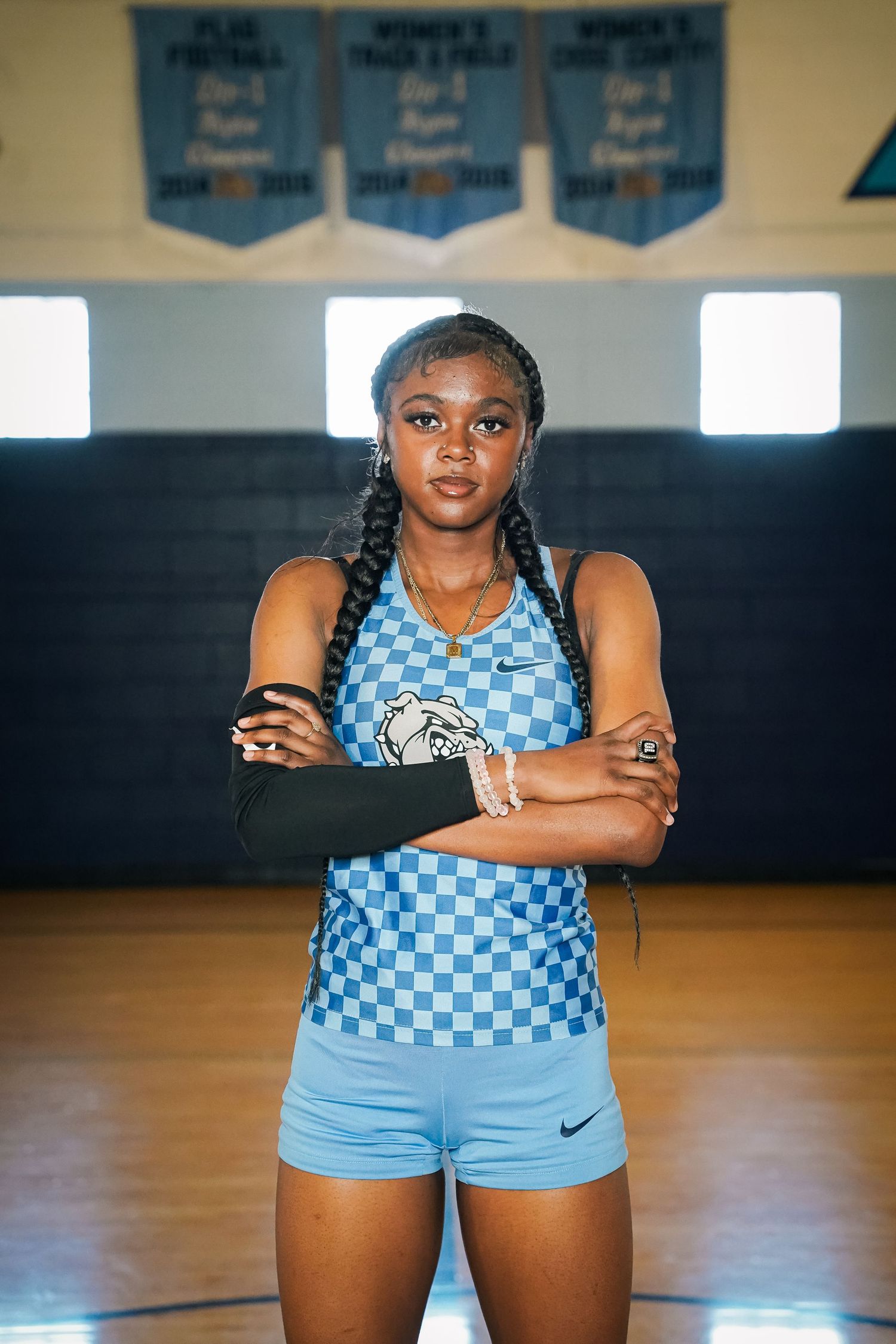 Athlete poses confidently in blue checkered uniform in a gymnasium with championship banners on wall.