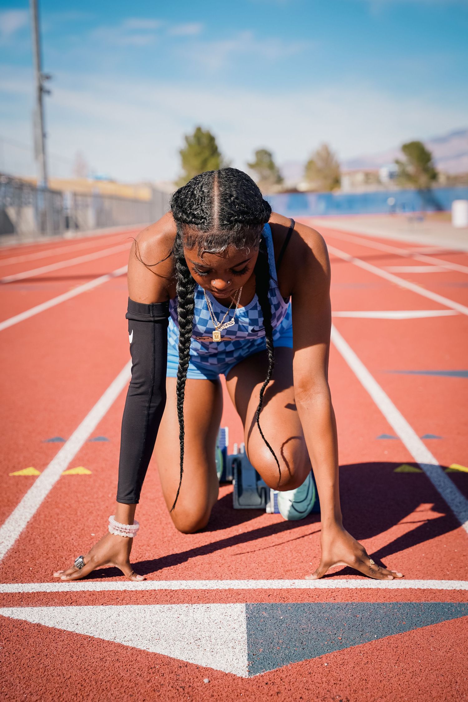 Athlete in racing stance on red track with protective arm sleeve.