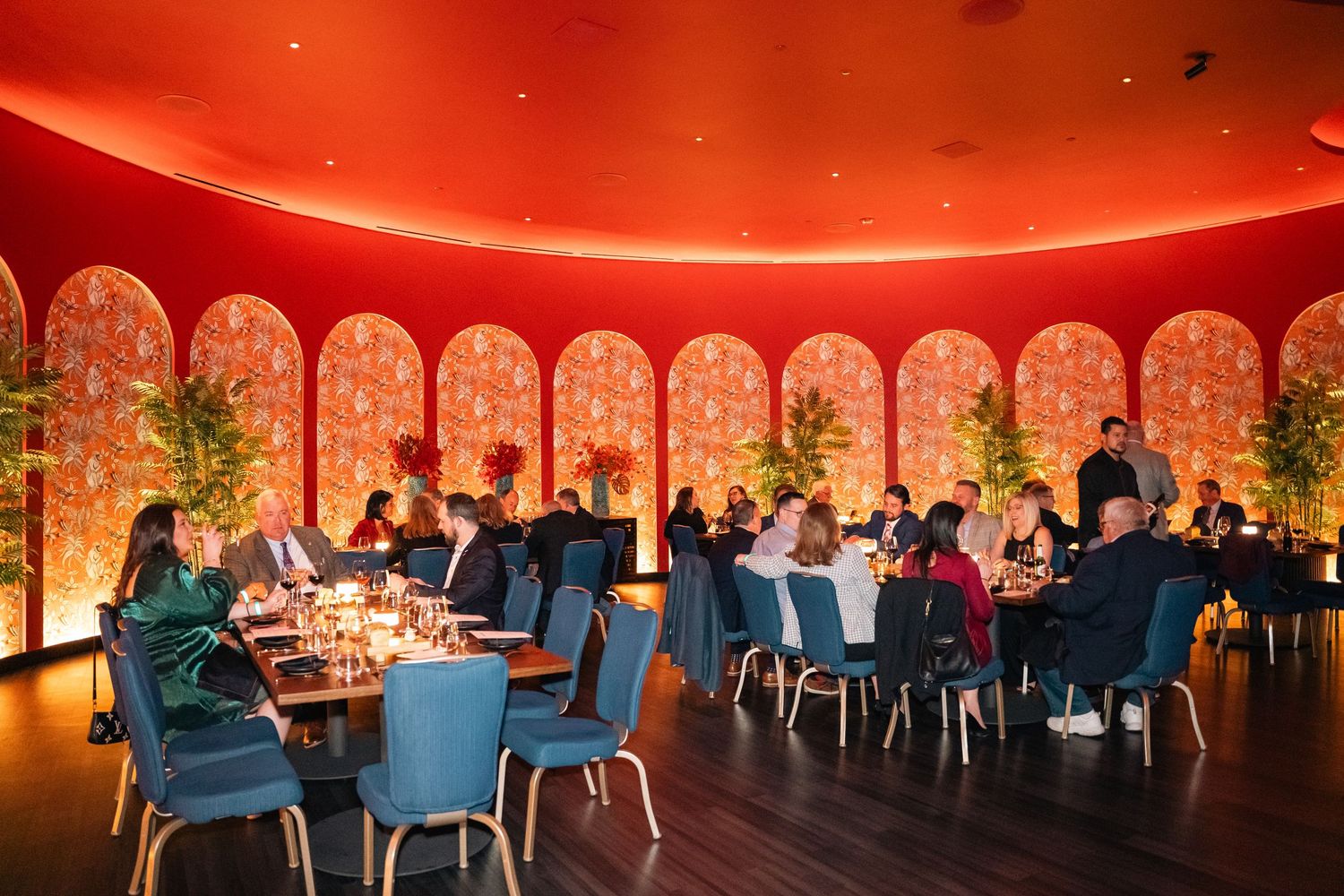Modern restaurant interior with curved ceiling, red lighting and guests seated at round tables.