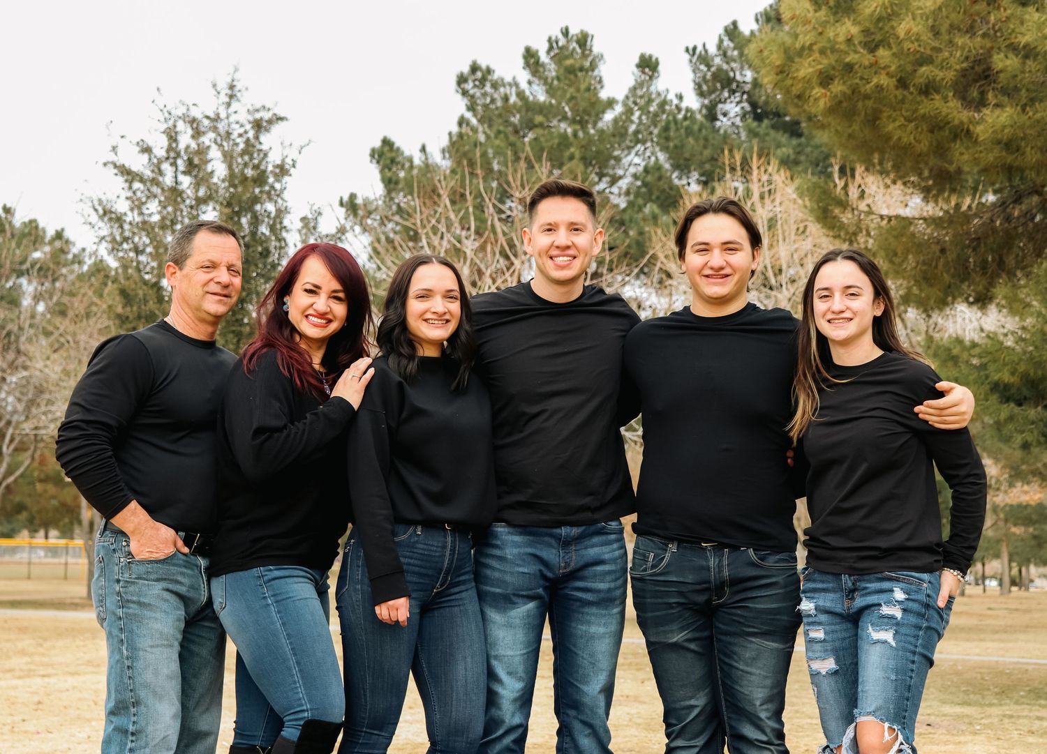 Family group wearing coordinated black outfits pose together for a portrait outdoors.