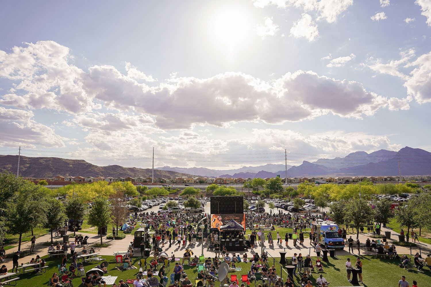 Aerial view of an outdoor festival venue with crowd gathered around stage surrounded by mountains and clear sky.