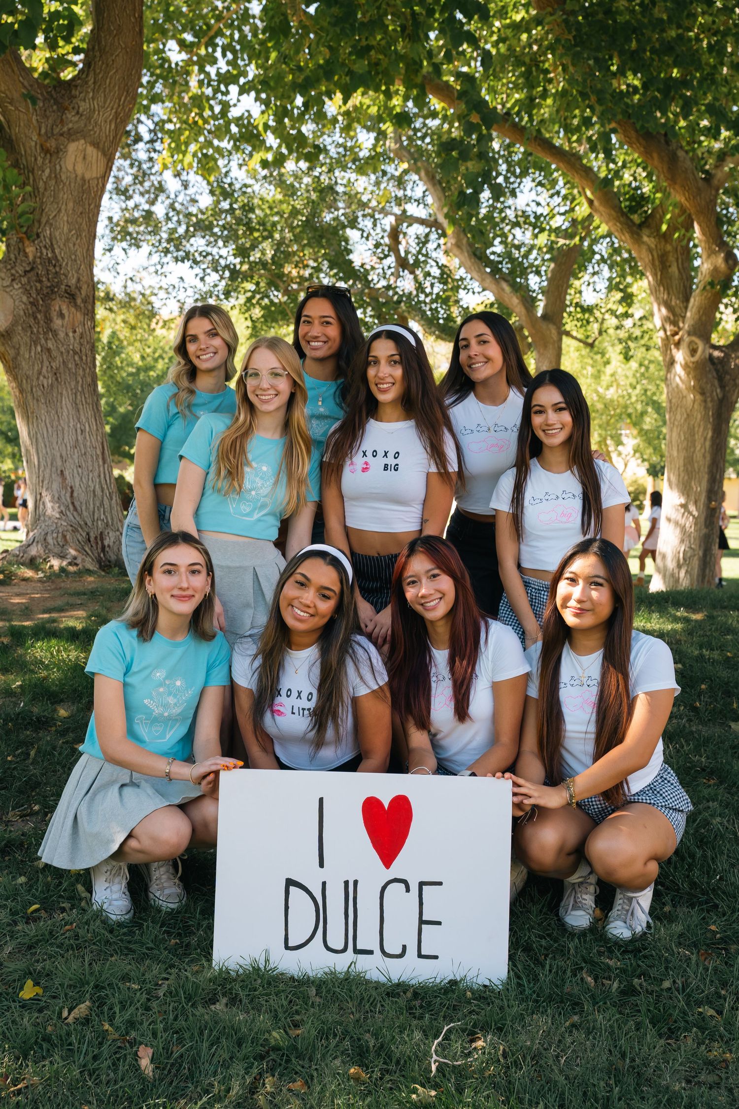 Group of sorority sisters in matching white t-shirts hold sign saying I love Dulce while posing outdoors.