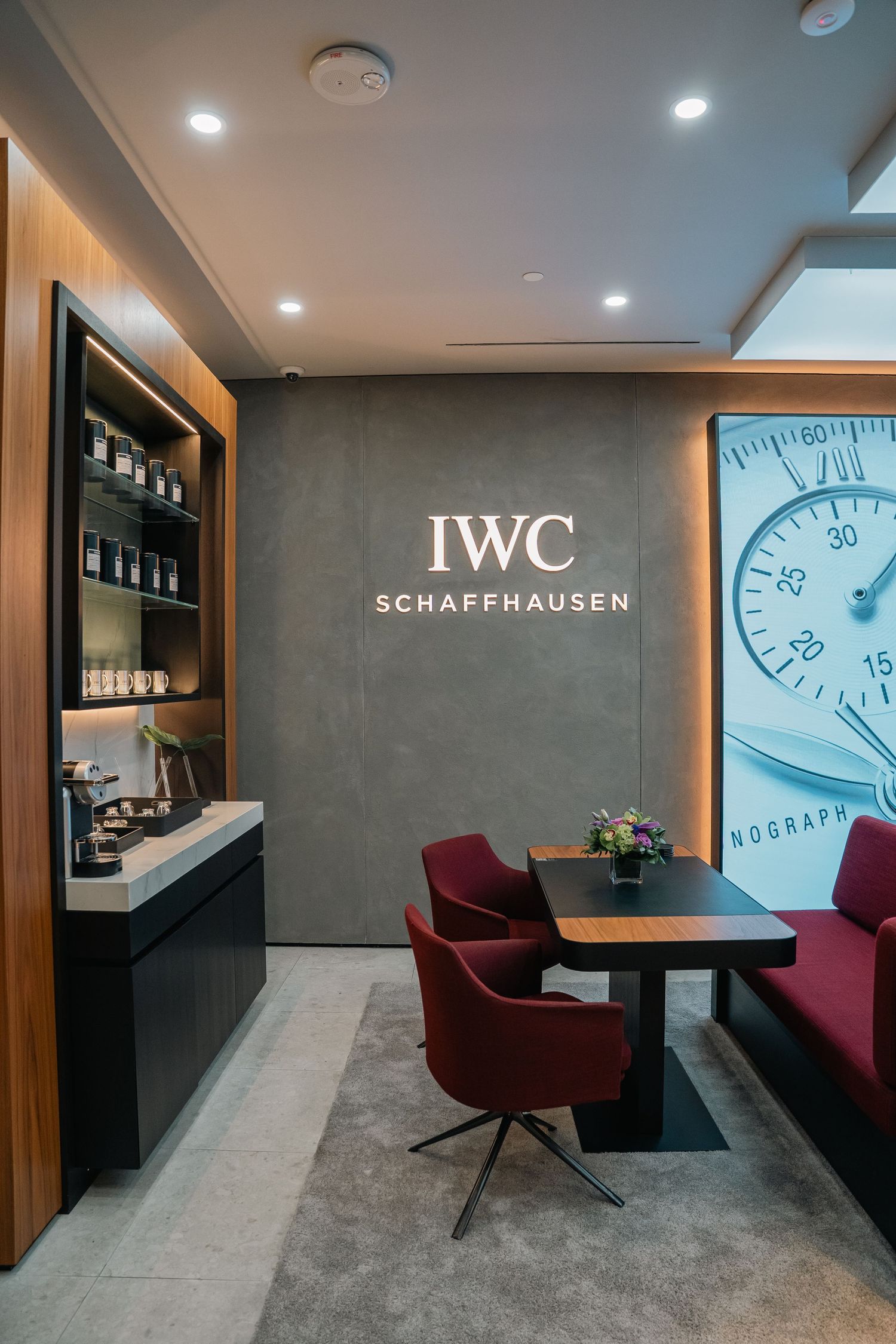 IWC Schaffhausen lounge area with clock imagery, grey walls, and burgundy seating.