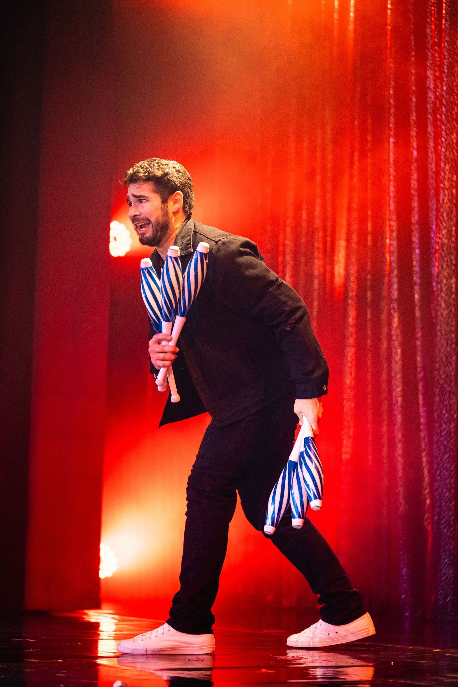 Entertainer in black outfit performing energetically on stage with red lighting.
