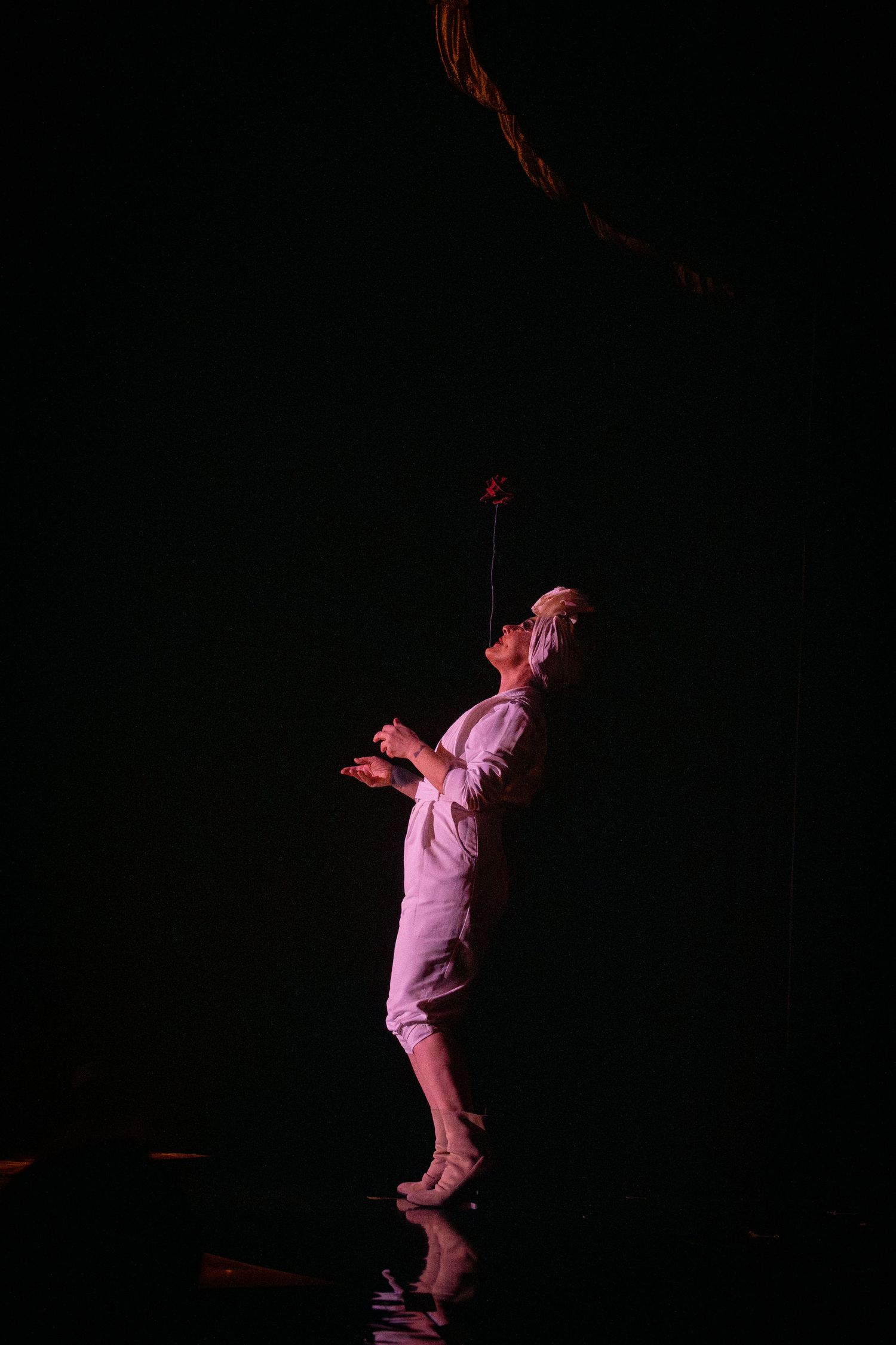 Performer in pink costume stretches upward during dramatic stage performance.