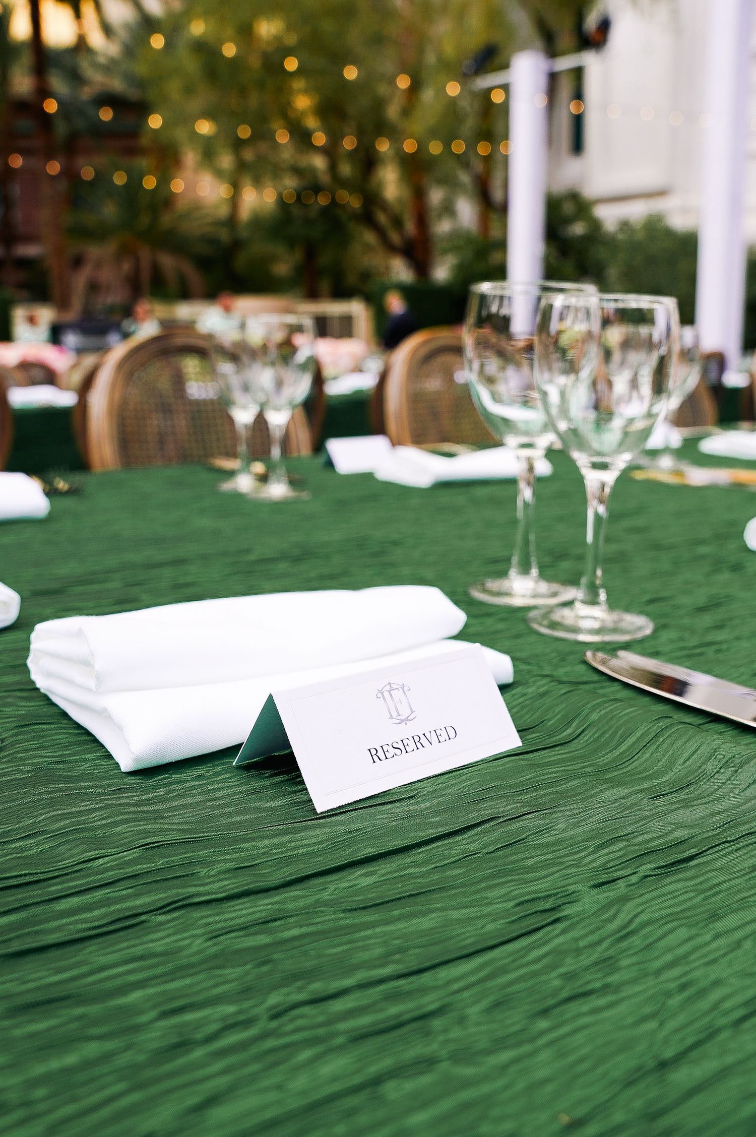 Close-up of formal place settings with white napkins and glassware on green crinkled tablecloth.