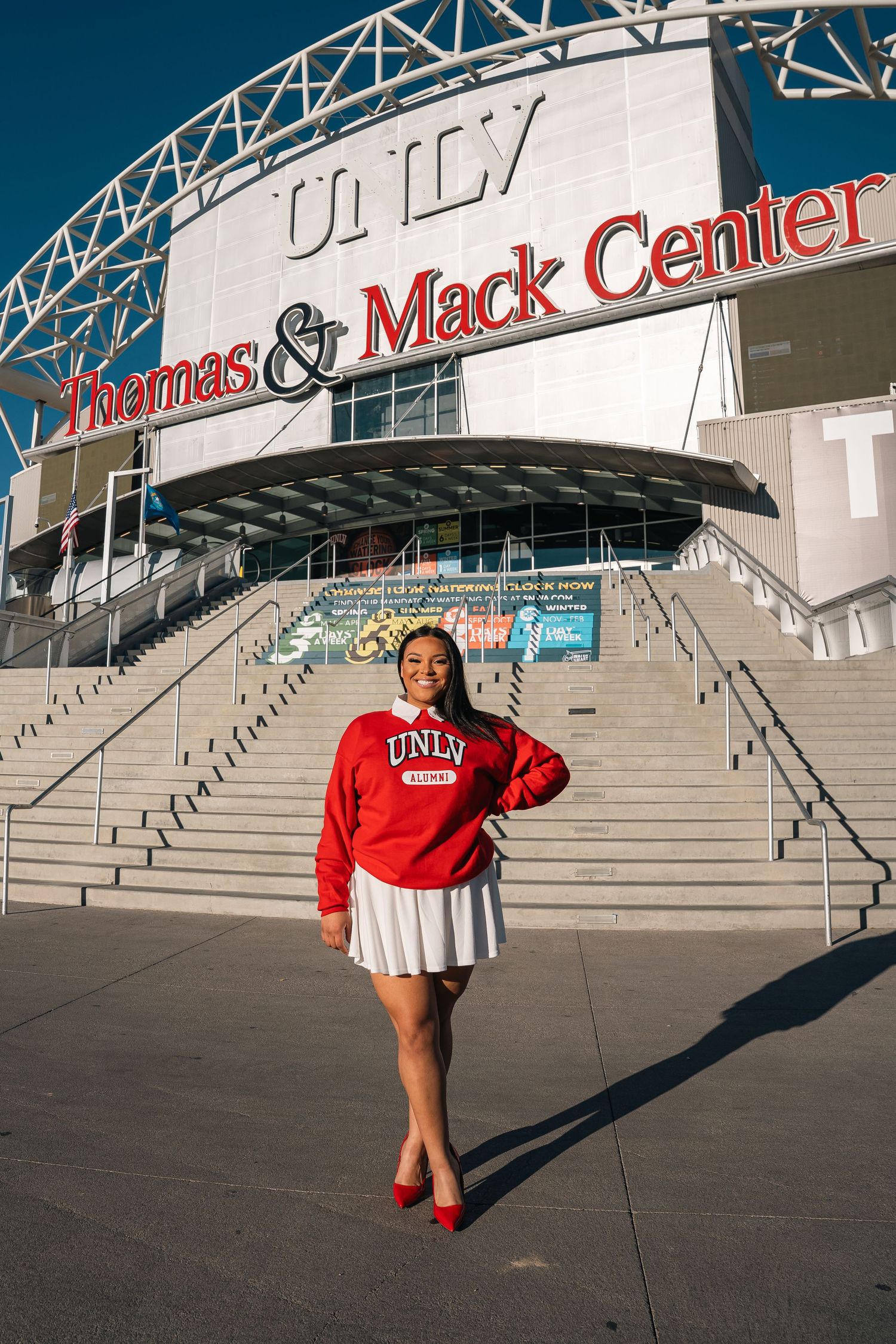 Monaco Media. Person posing in red university sweatshirt outside Thomas & Mack Center entrance stairs.