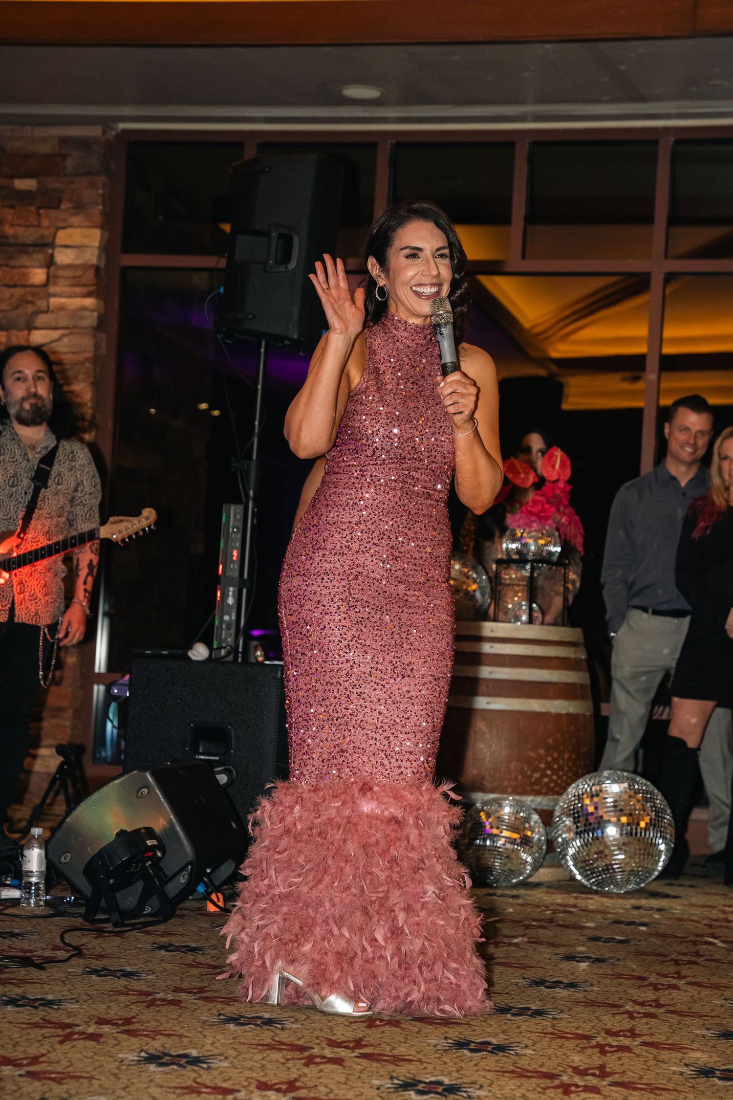 Performer in sparkly pink gown singing on stage with band.