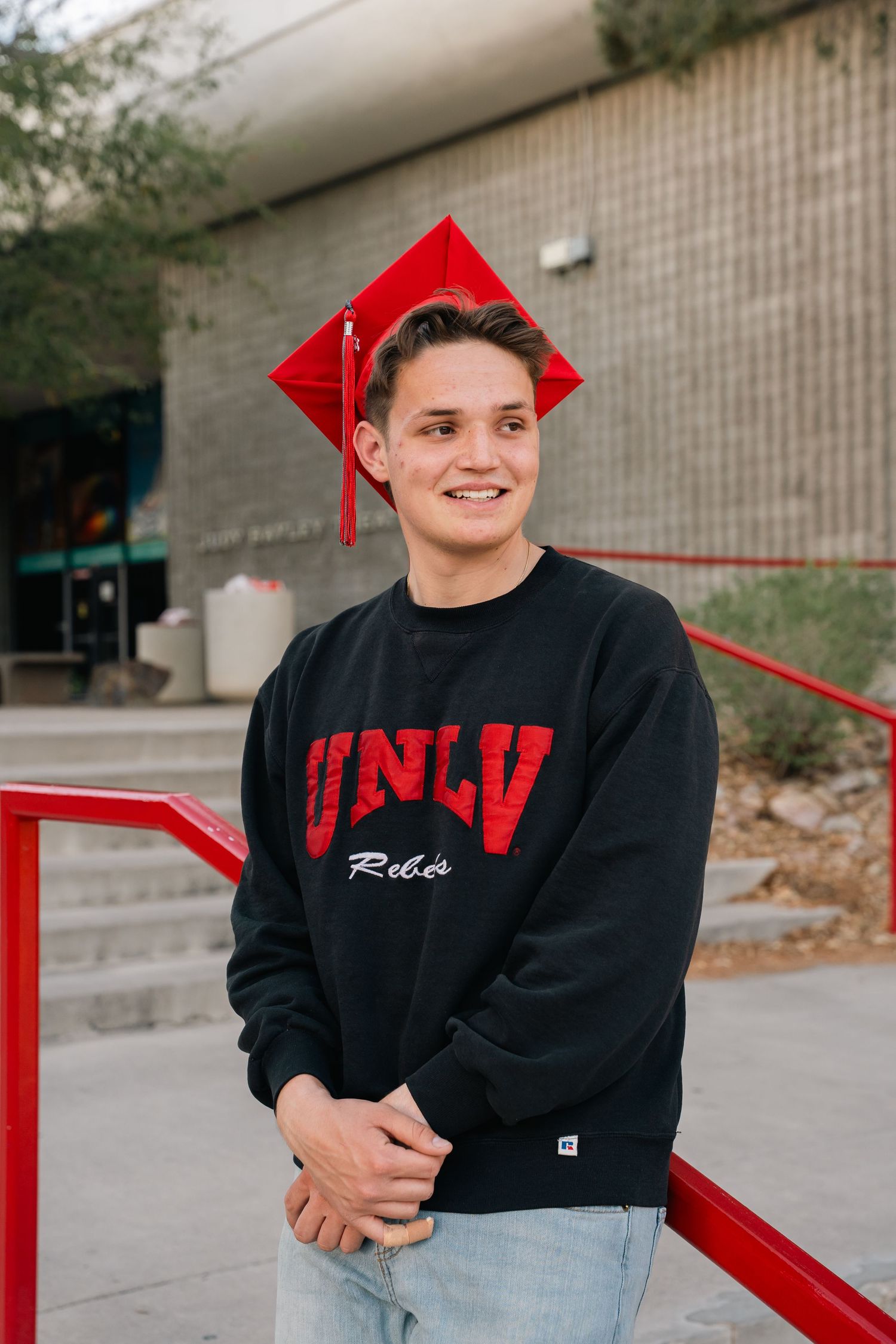 Graduate wearing red cap and UNLV sweatshirt poses on campus steps.