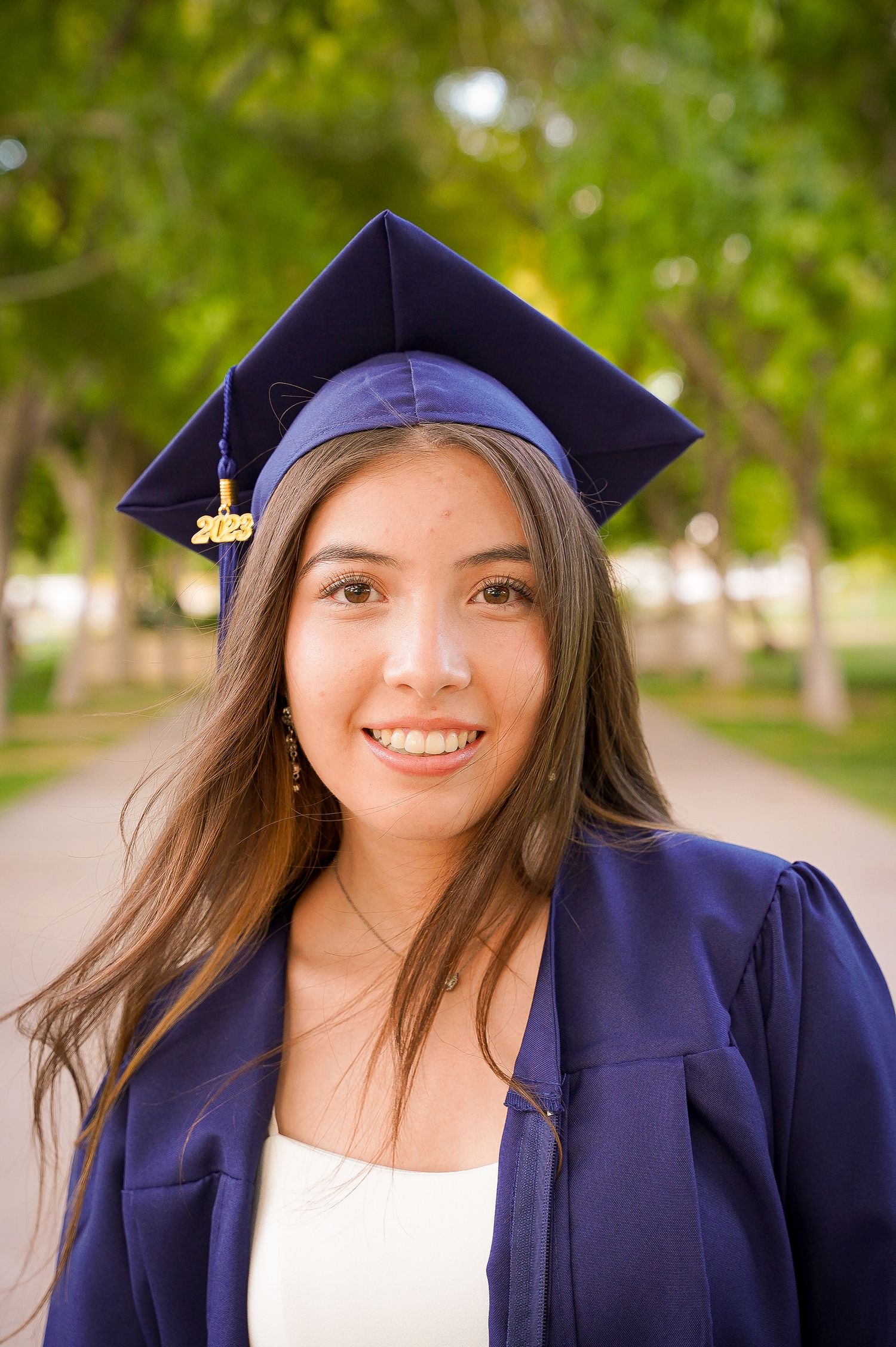 Close up portrait of graduate wearing purple graduation cap and gown with trees in background.