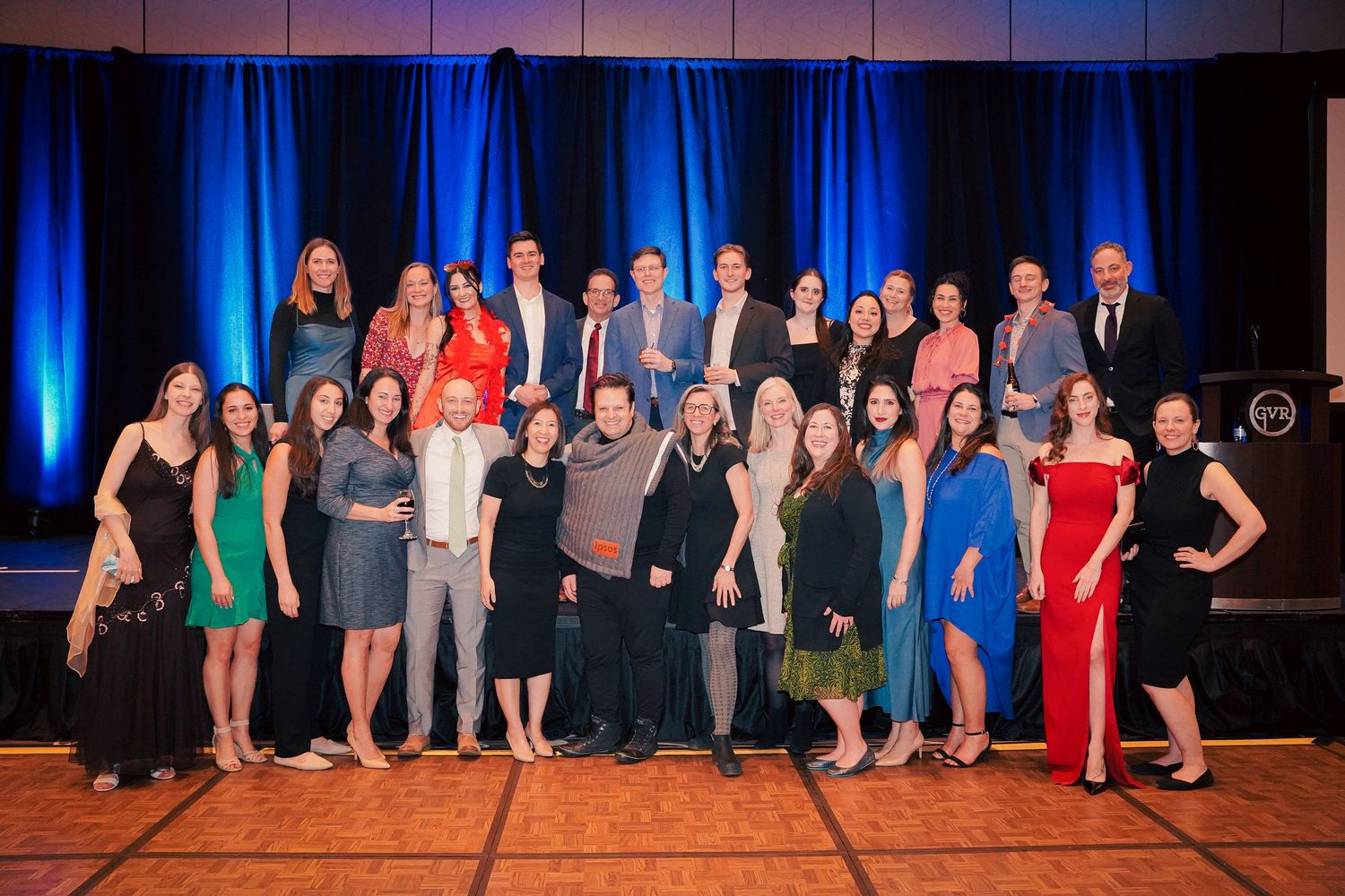 Large group portrait of formally dressed people posing together on stage with blue lighting.