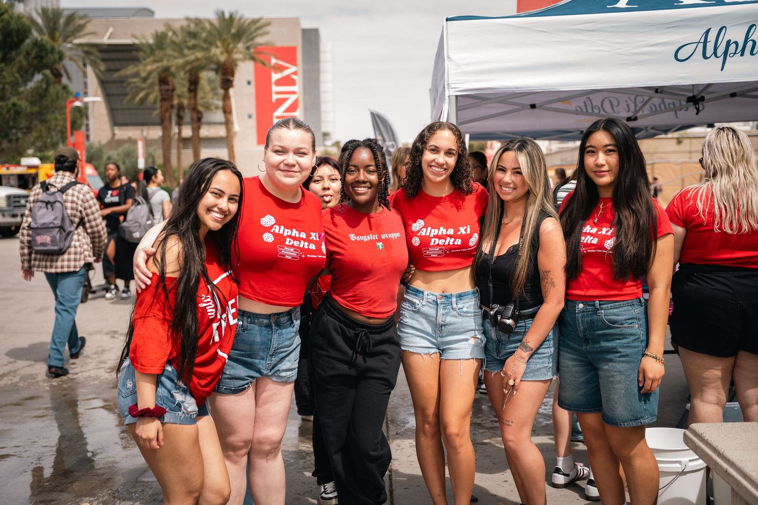 Group of friends in matching red shirts and denim shorts posing together at an outdoor event.