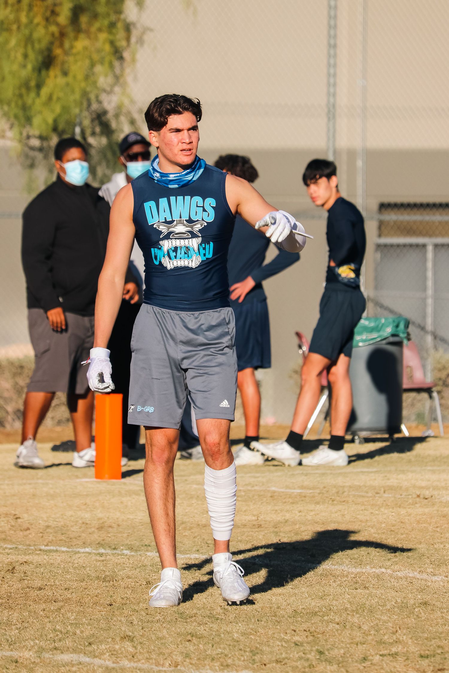 Athletic player in blue Dawgs jersey and gray shorts standing on sports field during practice.