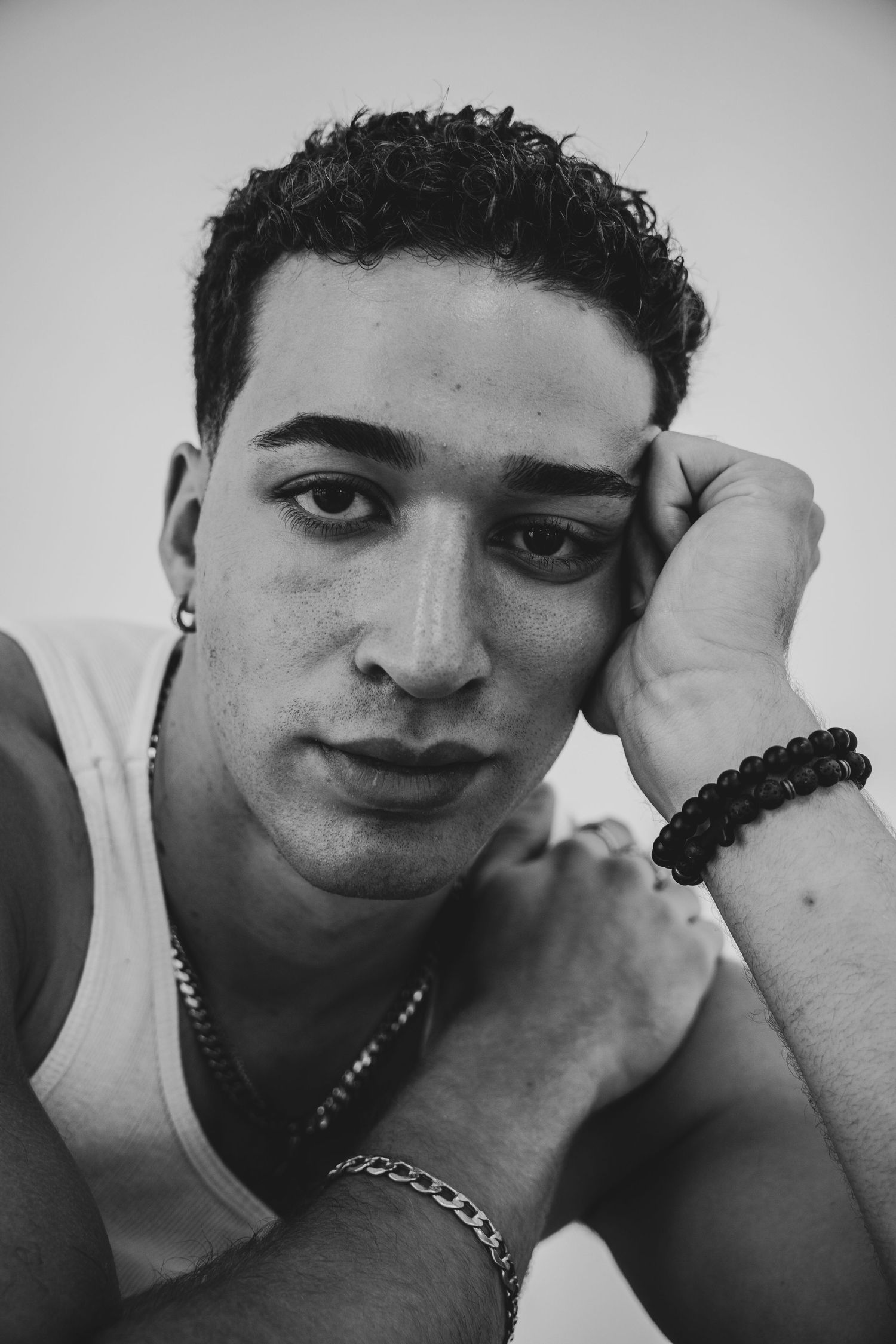 Artistic black and white headshot of a model wearing jewelry and a white tank top.