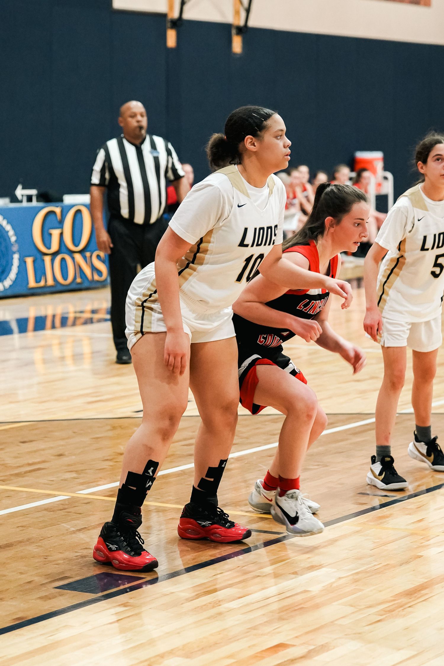 Basketball players from Lions and opposing team battle for position during an indoor game.