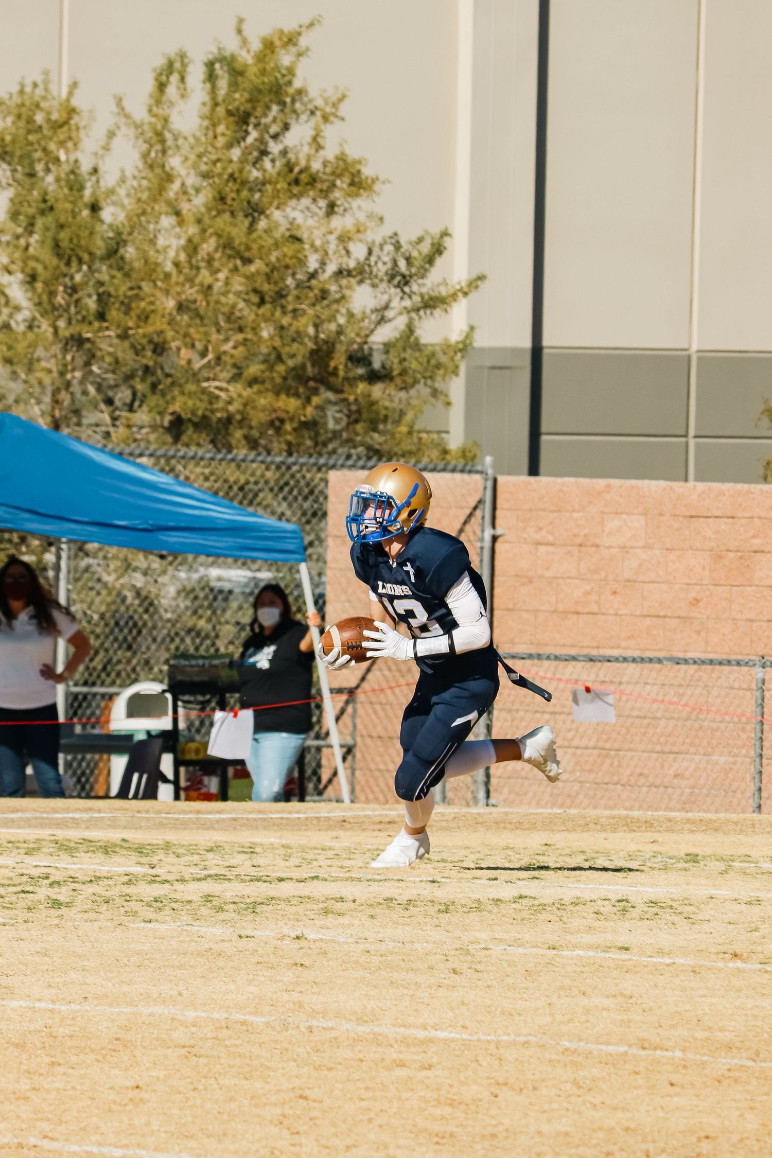 Football player leaping to catch ball during game with blue tent visible in background.