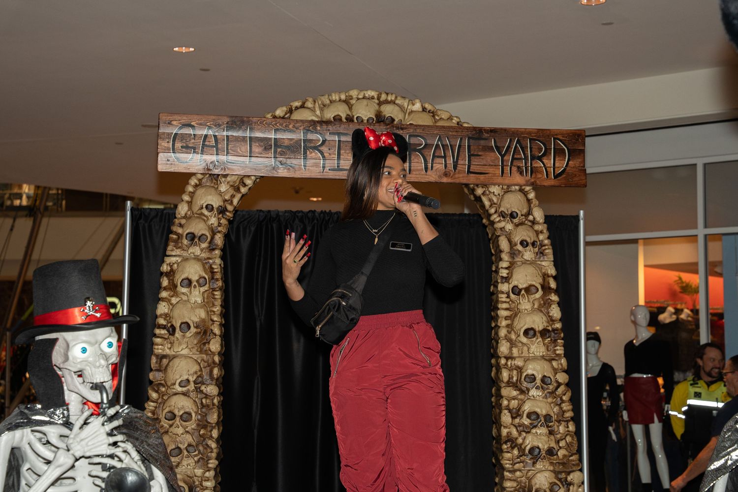 A person in black clothing climbs up a gold-decorated Halloween archway display at what appears to be a mall event.